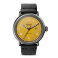 The Shinola Runwell Automatic Watch - Ochre features an ochre vellum-textured dial with black numerals, a date window at 3 o'clock, and a black leather strap. "Shinola" and "Automatic" are printed on the watch face.