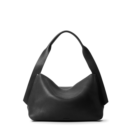 The Shinola Medium Derby Shoulder Bag - Black is crafted from natural grain leather with a wide, curved strap, zip closure, and a soft, slouchy shape, shown against a plain white background.