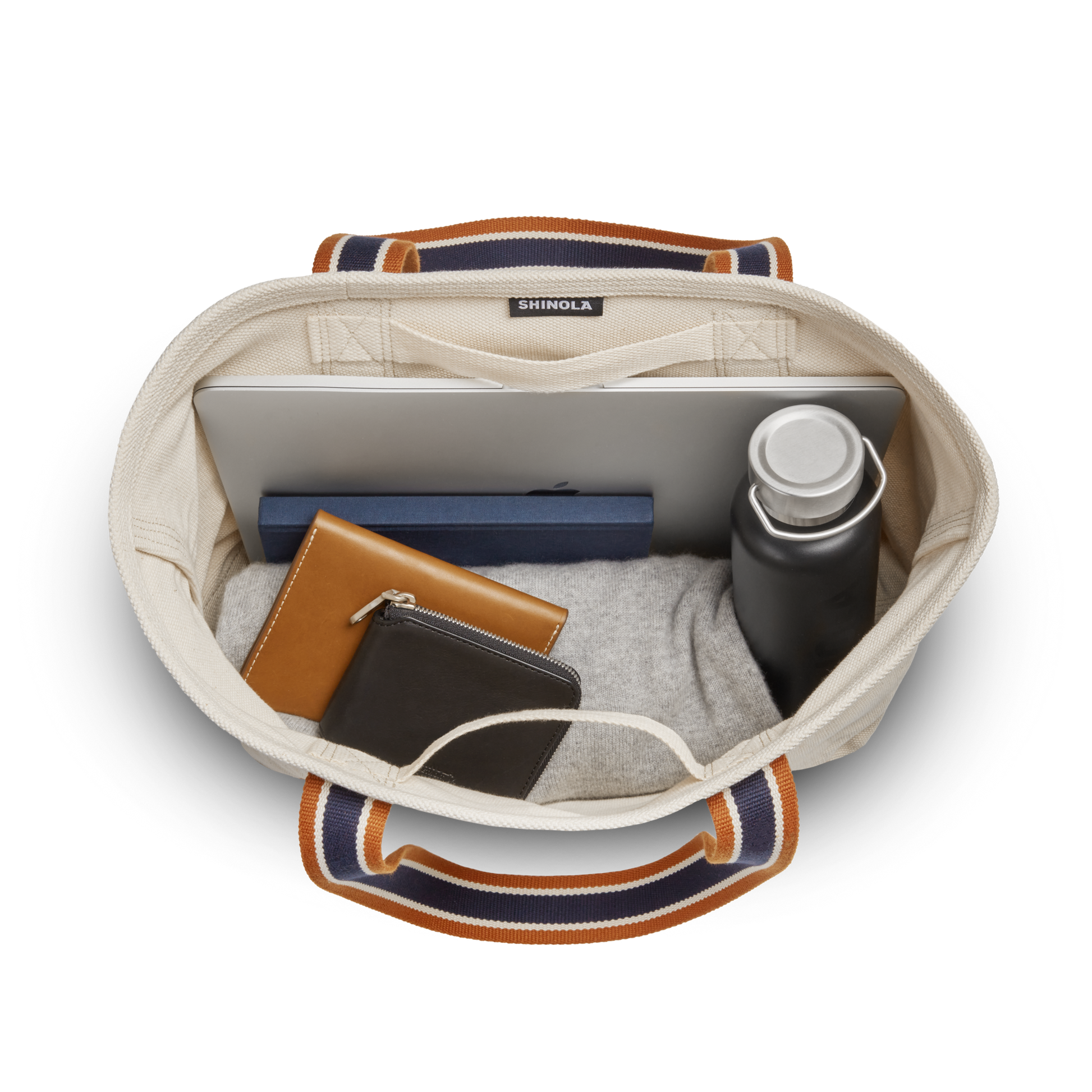 Overhead view of the Shinola Small Easy Canvas Tote - Natural with striped handles, holding a laptop, wallet, and water bottle—an ideal small tote for keeping essentials organized on the go.