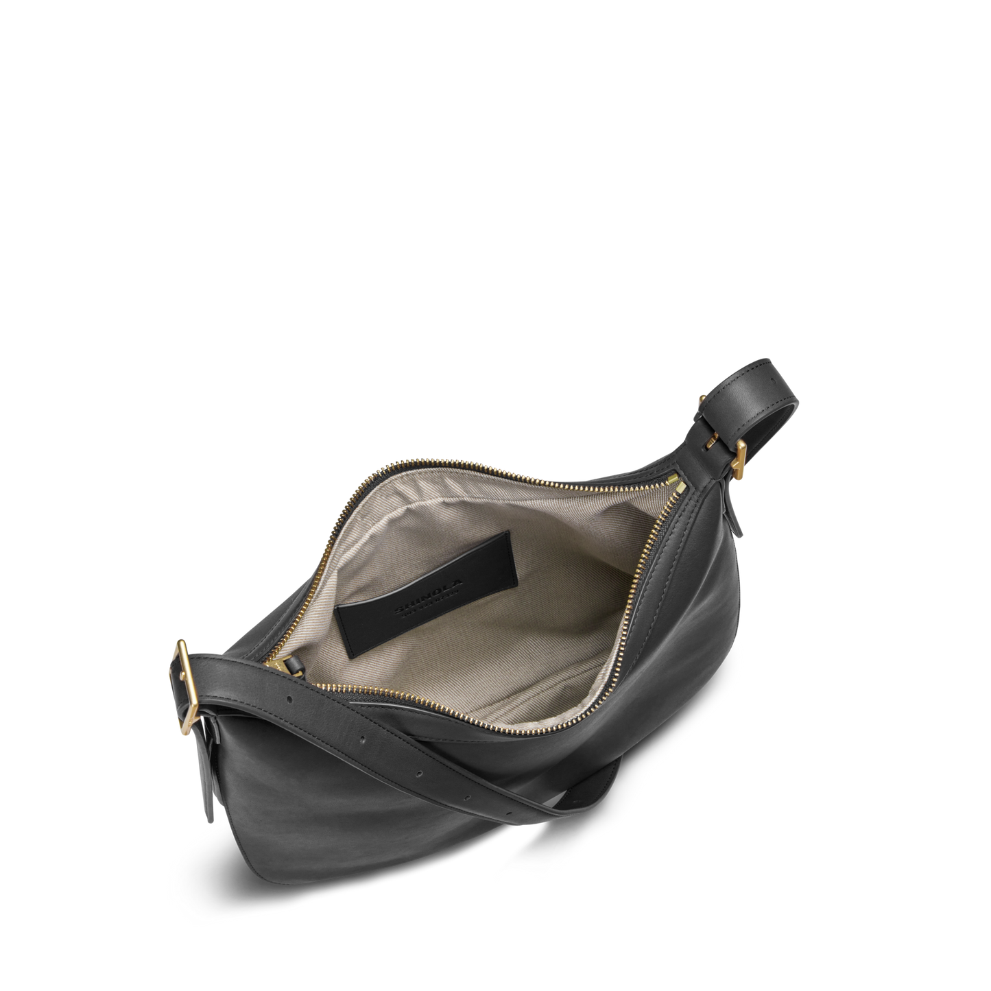 The Shinola Bixby Shoulder Bag - Black features natural leather, accordion design, gold zipper, beige fabric lining, small inner pocket, black label, and an adjustable strap with a gold buckle.