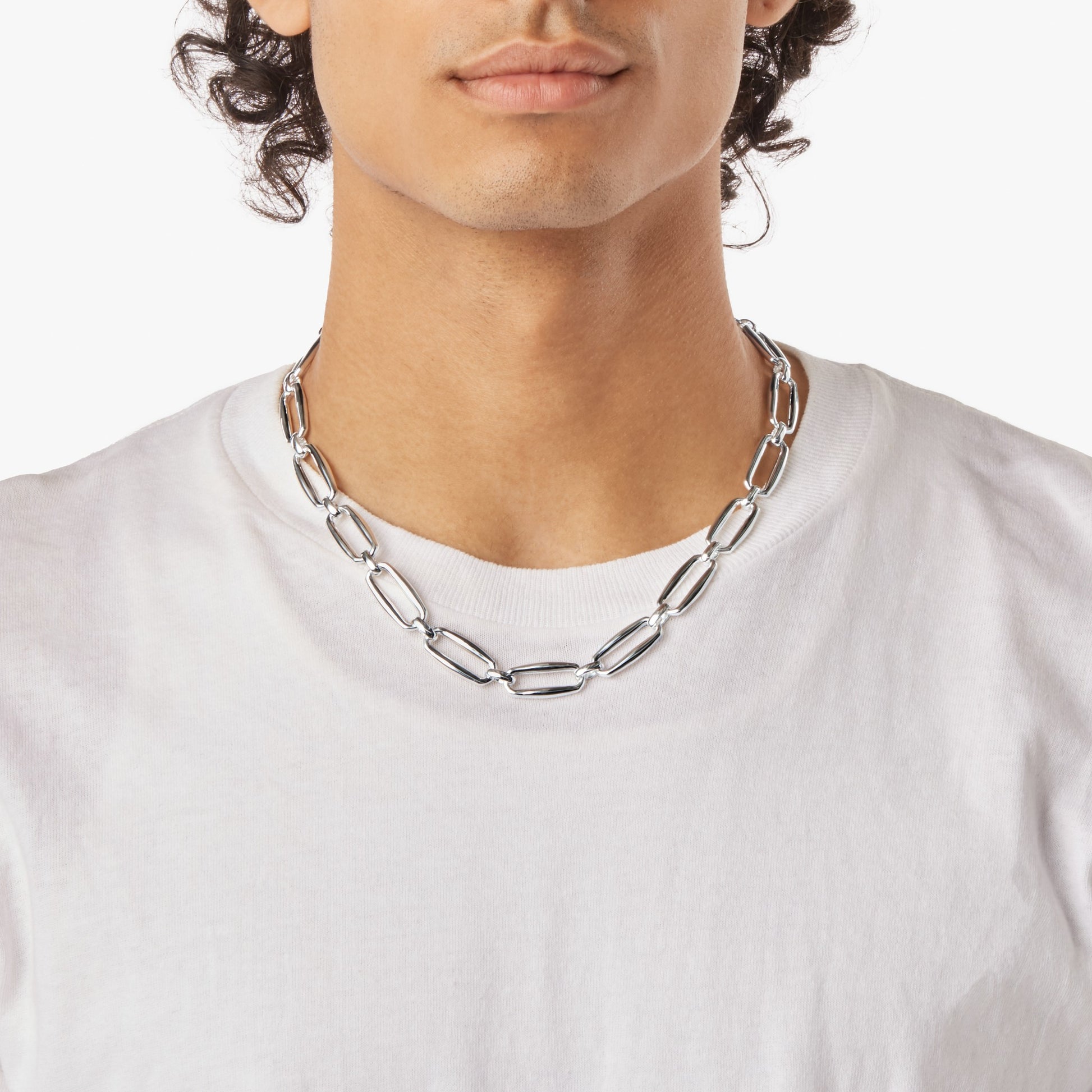 A person wearing a plain white t-shirt and the Shinola Signature Chunky Link Necklace in sterling silver, featuring large oval links, shown from shoulders to just above the mouth against a white background.