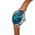 The Shinola Canfield Watch features an astro blue dial with white hour markers, a date display, a stainless steel case, and a brown leather strap. The watch is angled on a white background, displaying the Shinola brand name on the face.