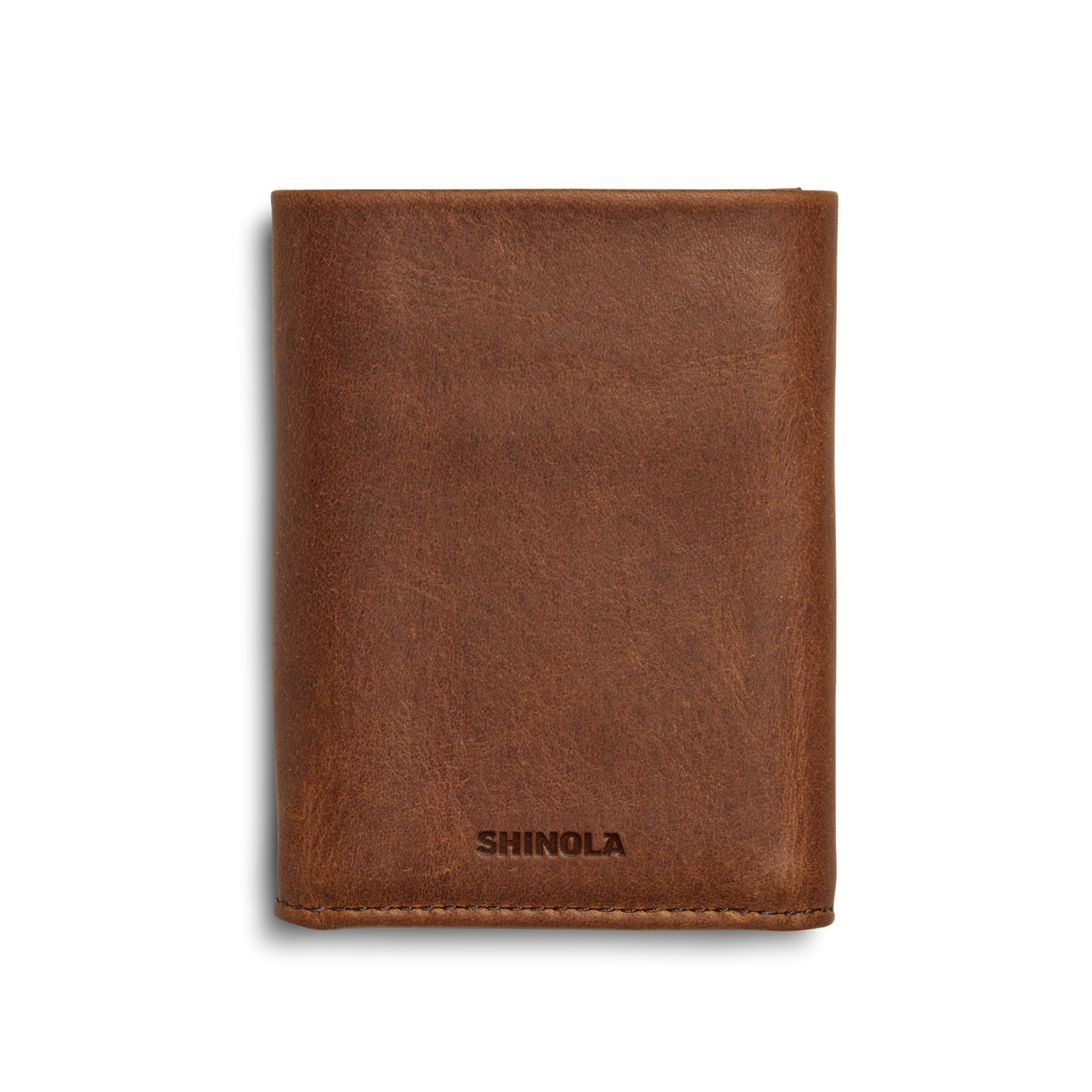 A medium brown Trifold Wallet by Shinola is shown closed, with "SHINOLA" embossed at the bottom center on the front against a plain white background.