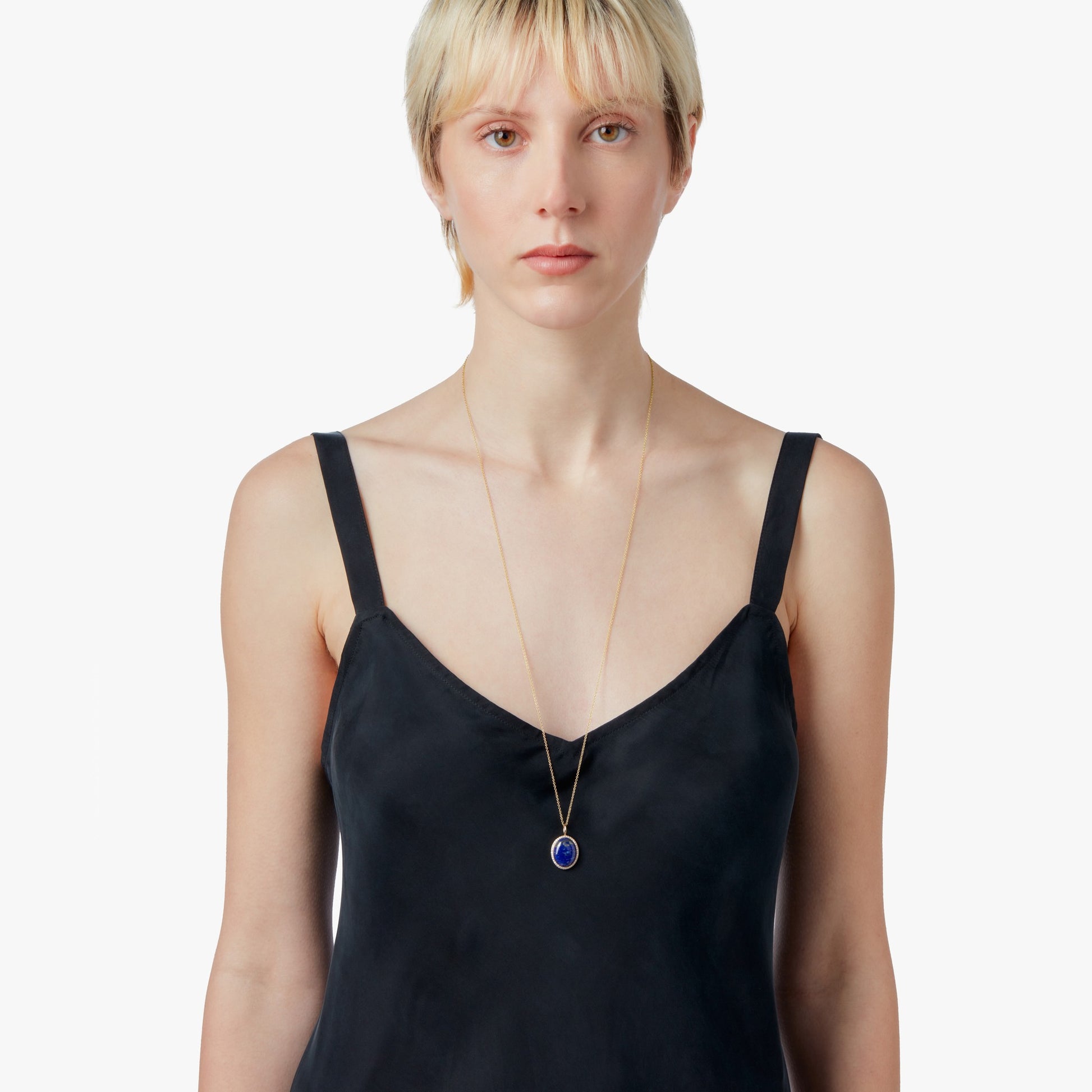 A woman with short blonde hair wears a black sleeveless dress and the Shinola Diamond Pave Lapis Pendant Necklace in yellow gold, standing against a plain white background.