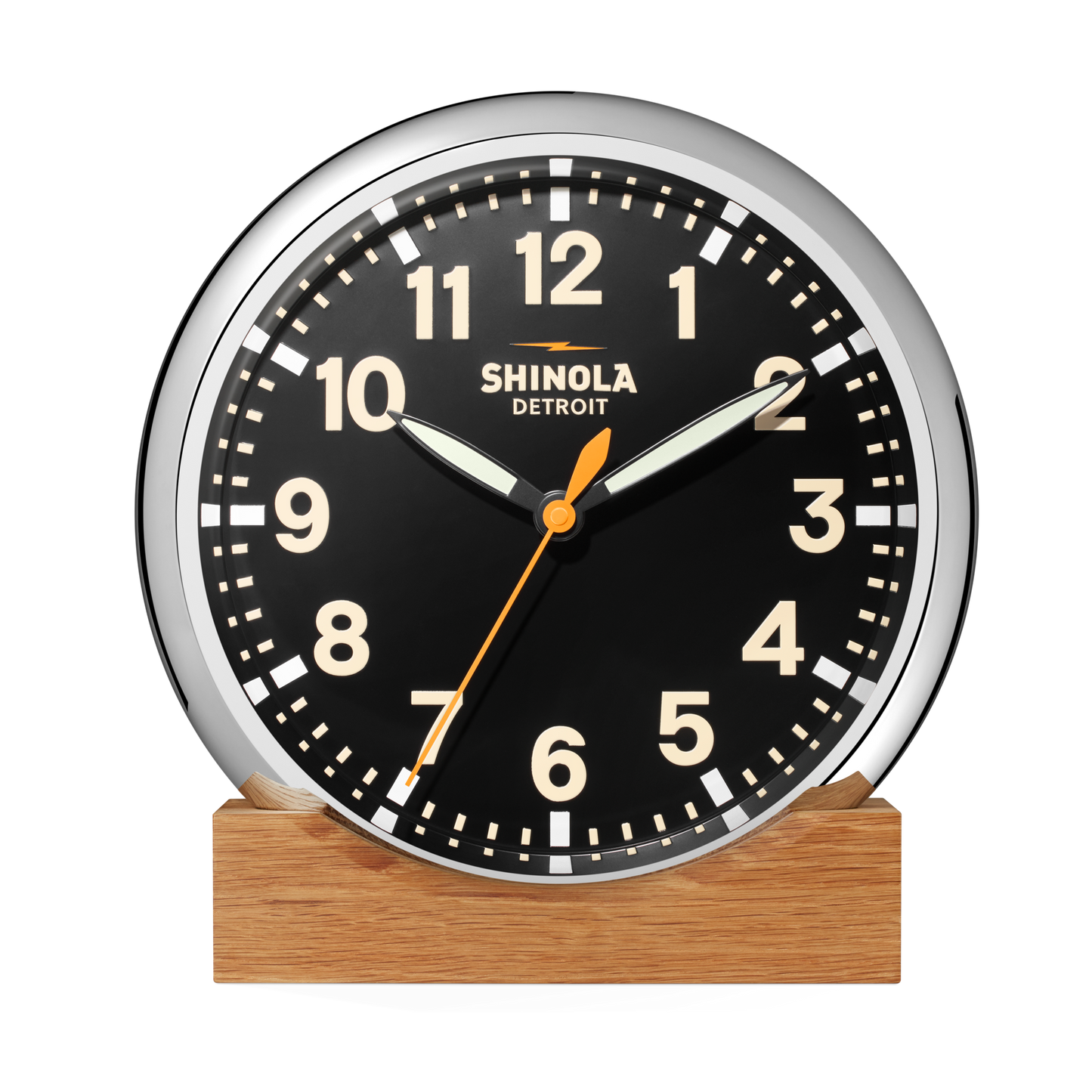 The 14" Runwell Clock - Black by Shinola features a black face, white numbers, chrome casing, and sits on a wooden base. The clock reads 1:52:34 and displays the Shinola brand name on its face.