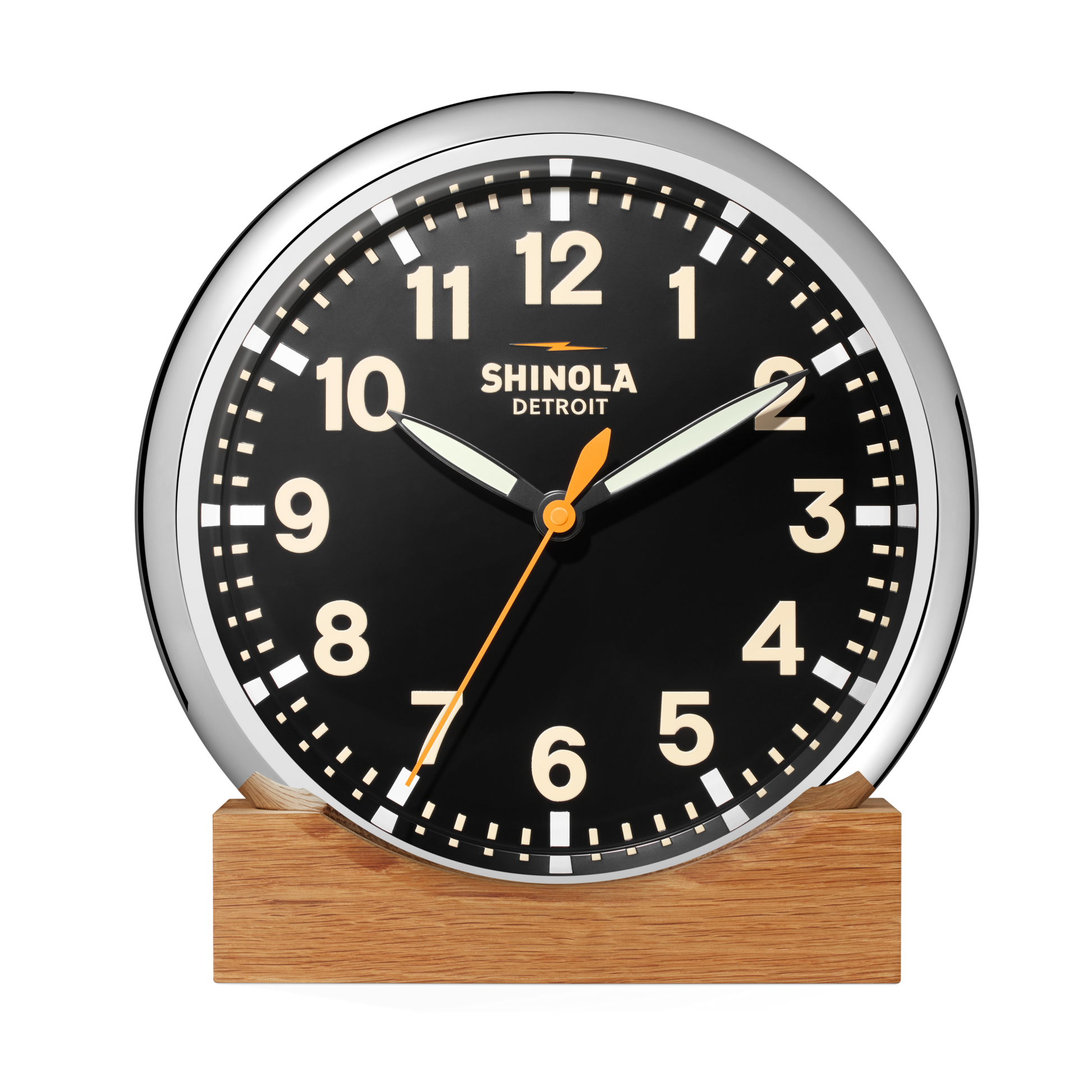 The 14" Runwell Clock - Black by Shinola features a black face, white numbers, chrome casing, and sits on a wooden base. The clock reads 1:52:34 and displays the Shinola brand name on its face.