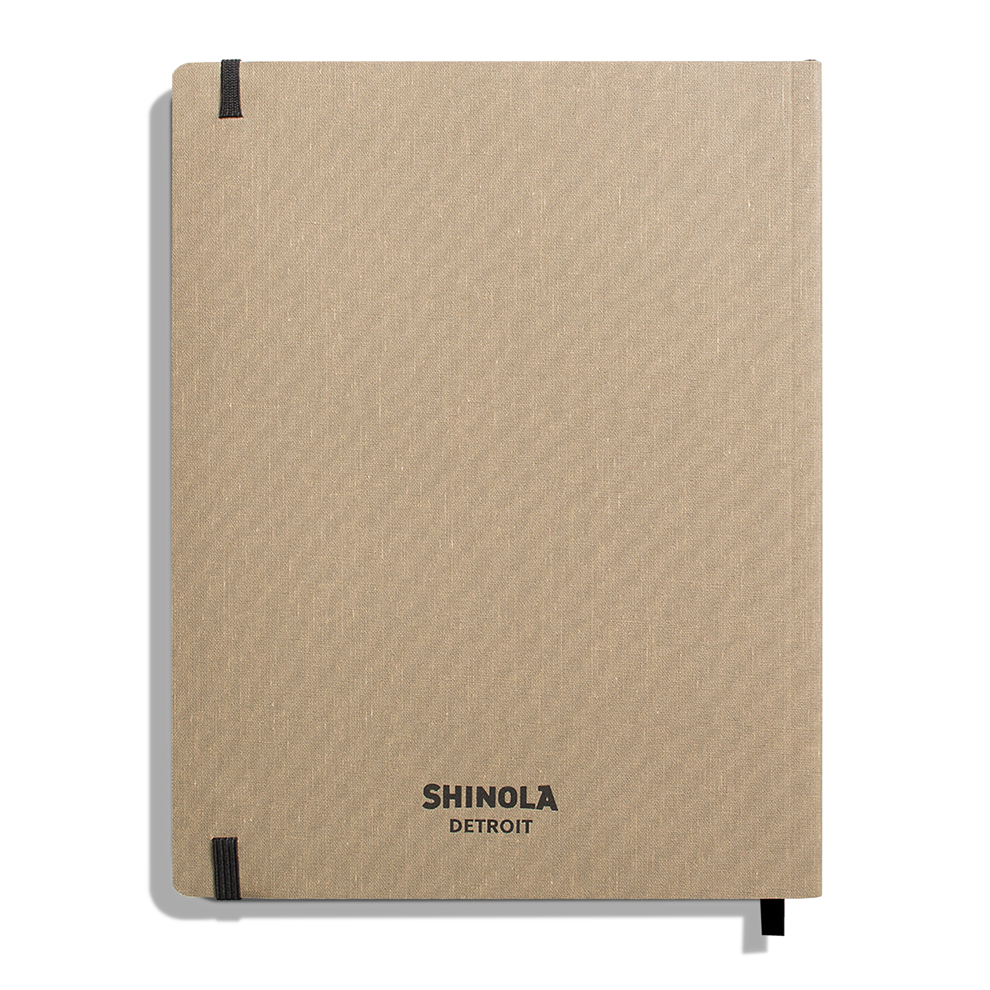 A large, oat-colored softcover ruled journal by Shinola, American-made, with black elastic bands at two corners and “Shinola Detroit” in black at the bottom center of the cover.