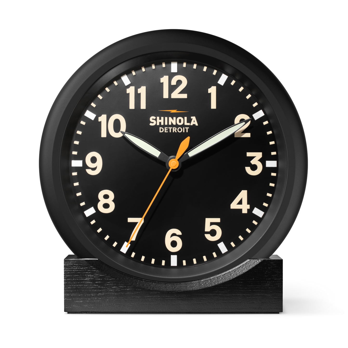 The Shinola 14" Runwell Clock - Black features a matte black dial with white numbers, hands, an orange second hand, "Shinola Detroit" on the face, and sits on a matching rectangular base. The time shown is 10:10:35. Inspired by the Runwell Wall Clock.
