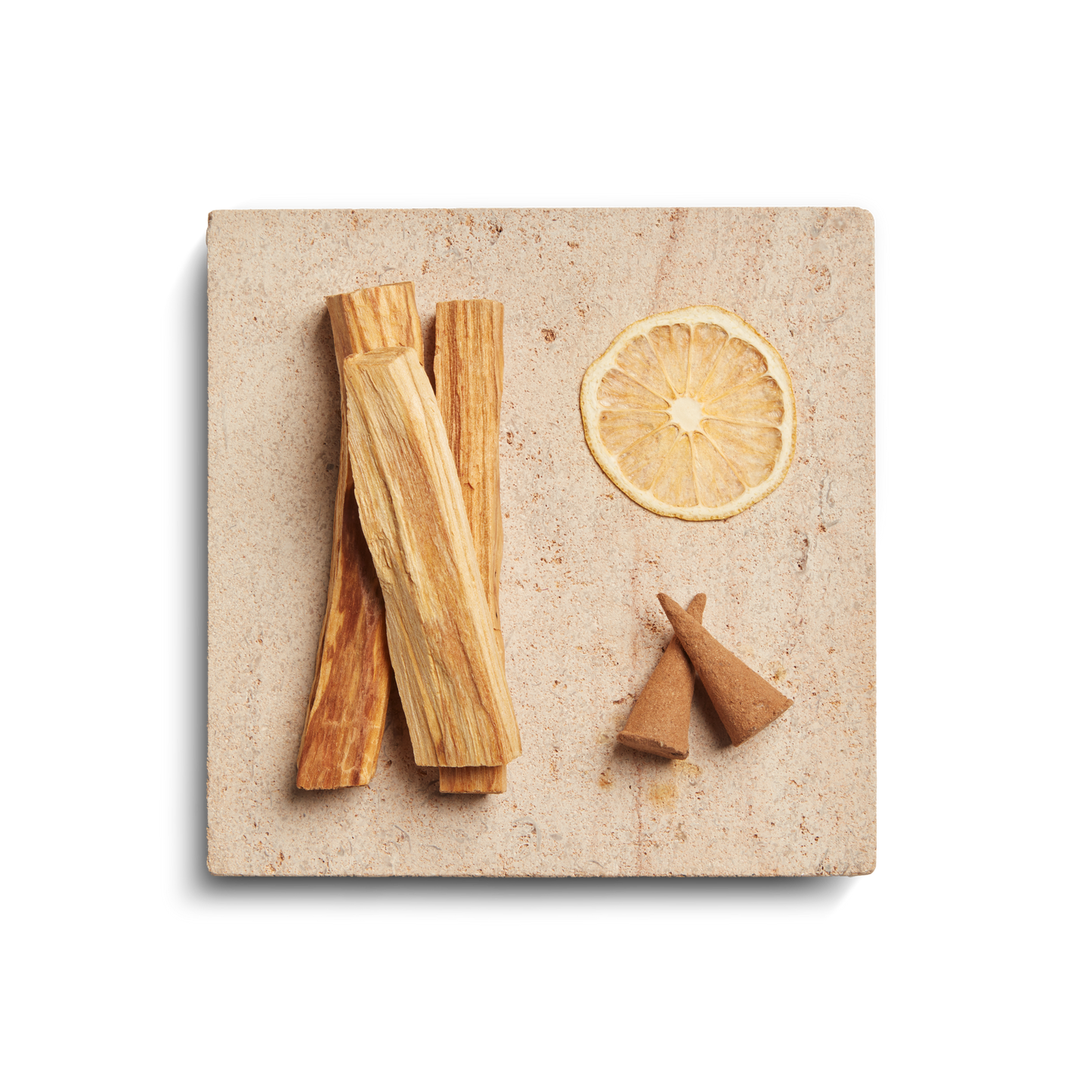 The Shinola Smoke 8oz Scented Candle sits on a square beige stone, paired with dried lemon, palo santo wood, and incense cones, creating a soothing woody aroma against a clean white background.