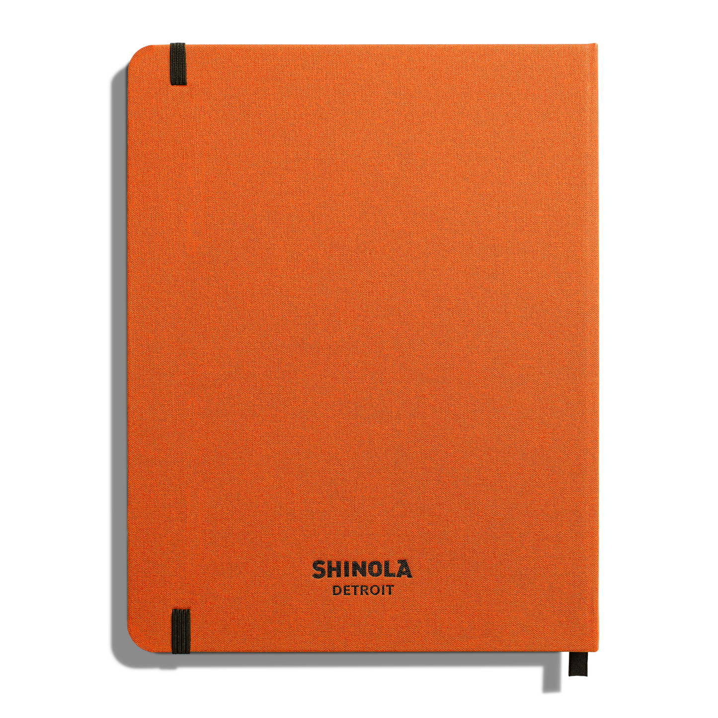 The Medium Hard Ruled Journal - Bold Orange by Shinola is a premium orange hardcover notebook with black elastic bands on two corners and "SHINOLA DETROIT" printed in black near the cover’s bottom center.