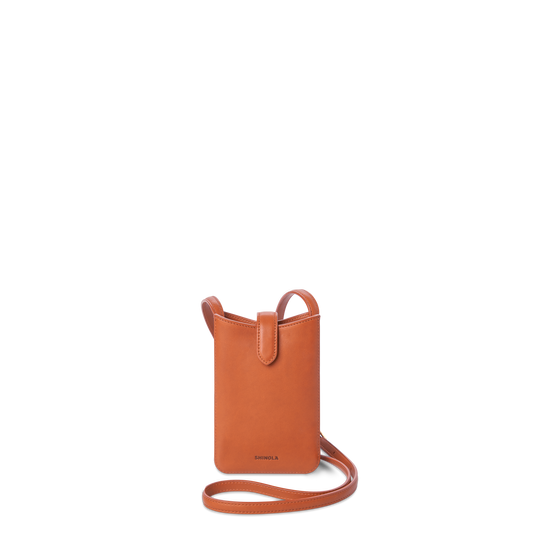 The Bixby Phone Crossbody - Rust by Shinola is a compact, rectangular bag in natural leather with a long strap and flap tab, featuring the Shinola logo embossed near the bottom.