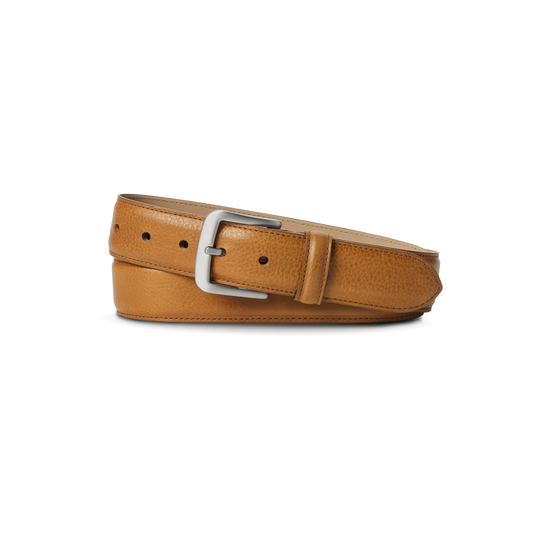 The Shinola 1 1/2" Canfield Belt in Bourbon is crafted from Italian Vachetta leather, showcasing a tan finish and silver rectangular buckle, neatly rolled and set against a plain white background.