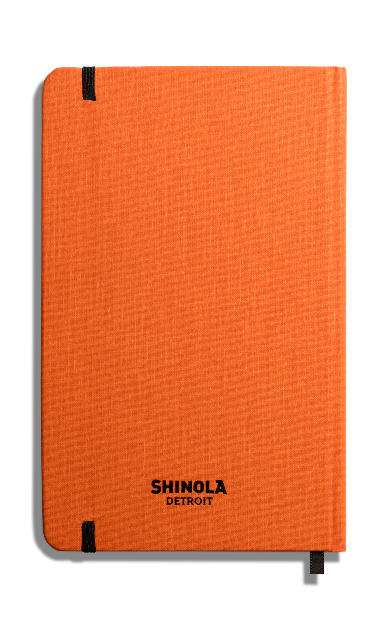 The Medium Hard Ruled Journal in Bold Orange by Shinola features a hard linen orange cover, black elastic bands, and "SHINOLA DETROIT" printed on the front. Made in the USA, it's shown against a white background.