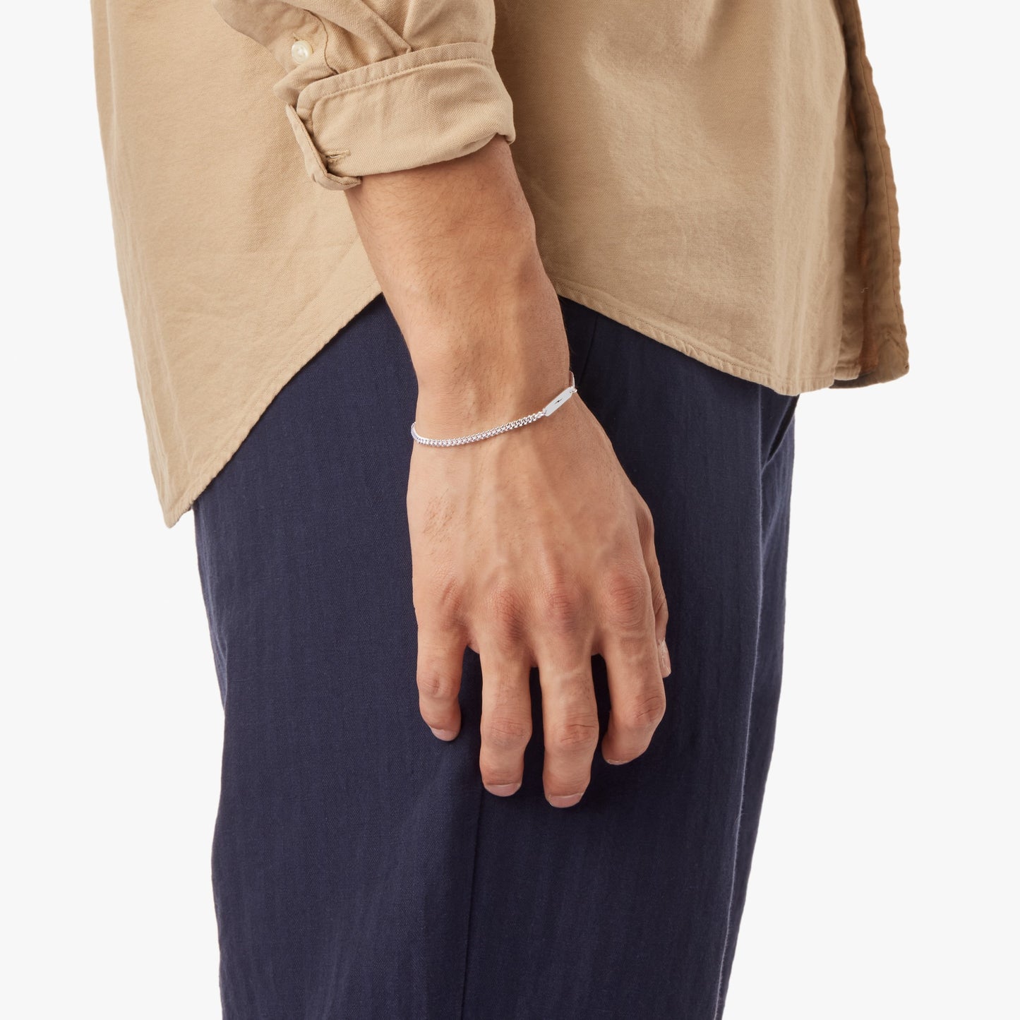 A person in a beige shirt and navy pants, shown from the waist down with their arm relaxed, wears the Shinola 3mm Gauge Chain Bracelet - Sterling Silver on their wrist.