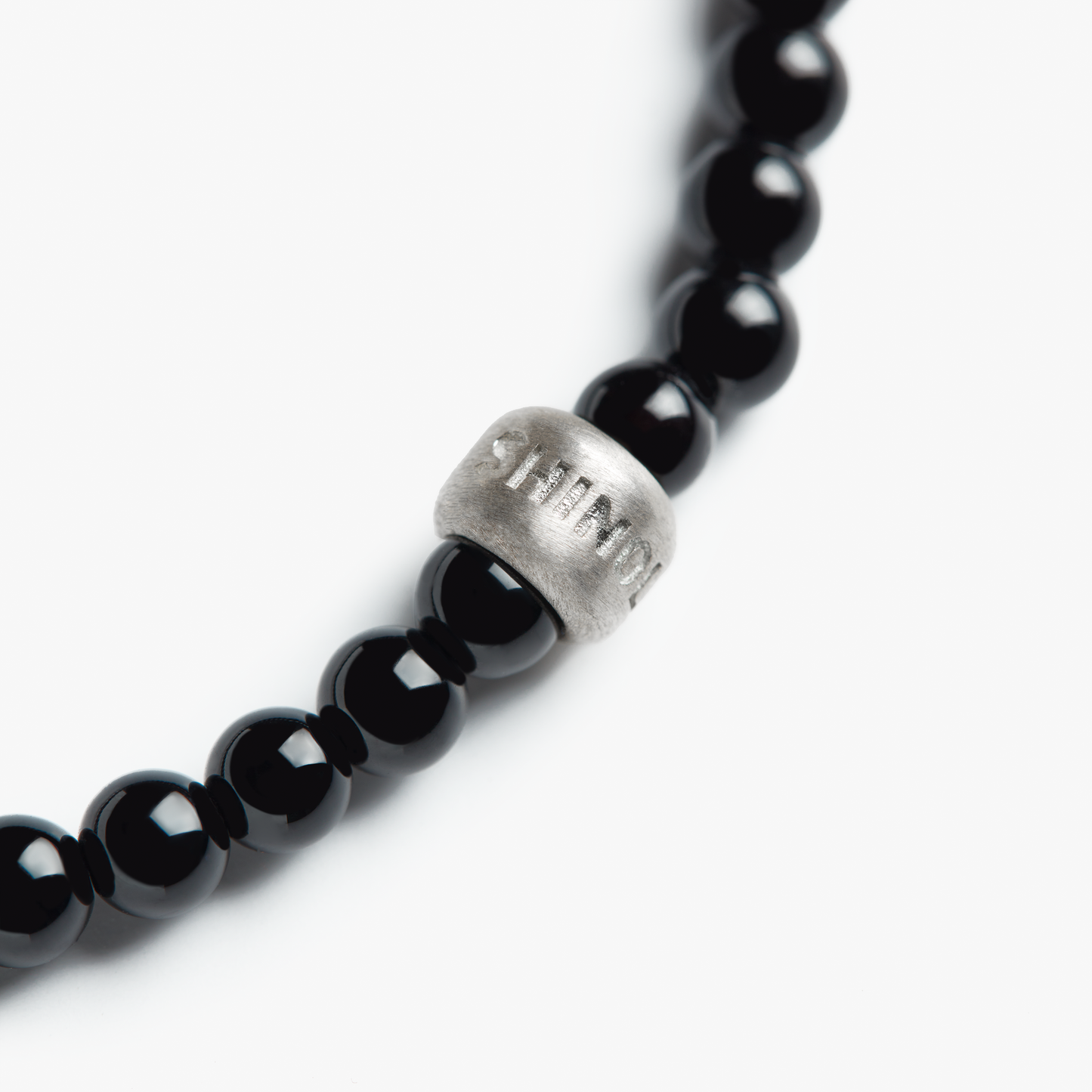 A close-up of the Shinola 4mm Beaded Onyx Bracelet, featuring polished onyx beads and a sterling silver accent bead engraved with "STAMOU," photographed against a white background.