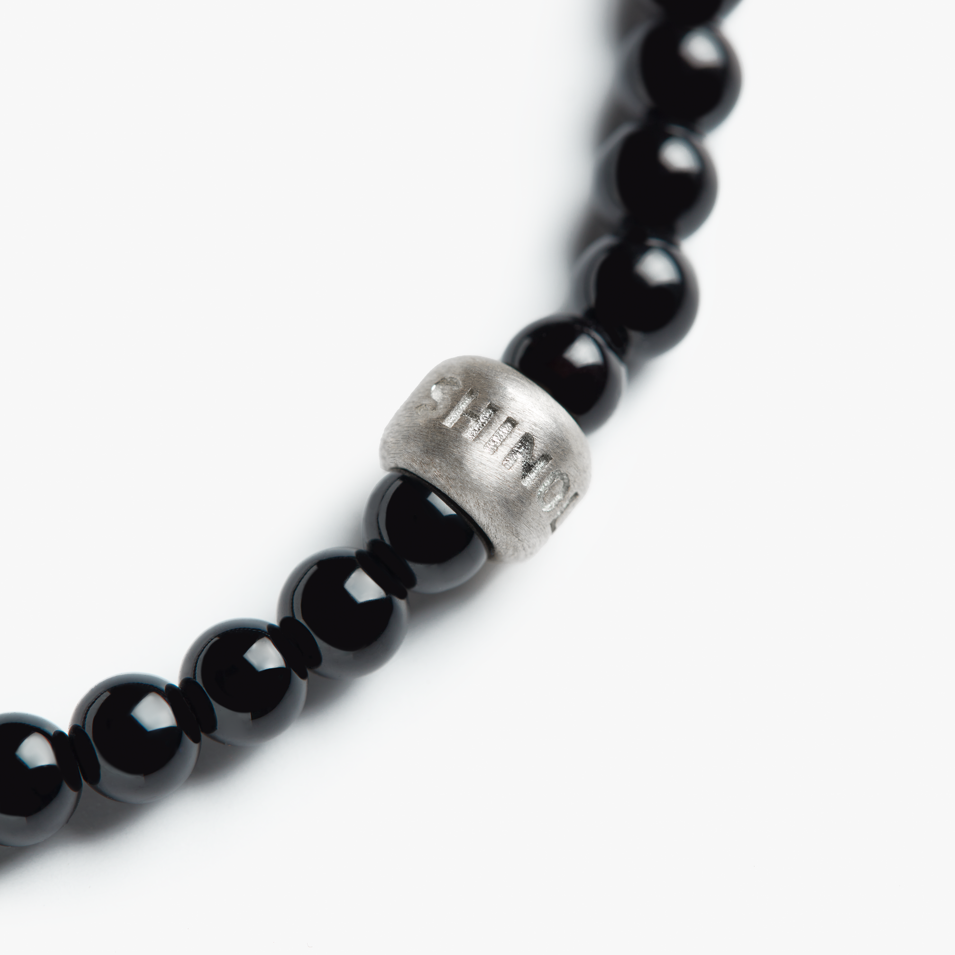 A close-up of the Shinola 4mm Beaded Onyx Bracelet, featuring polished onyx beads and a sterling silver accent bead engraved with "STAMOU," photographed against a white background.