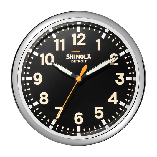 A Shinola 14" Runwell Clock - Black features a black face, white numbers, chrome casing, white hour and minute hands, an orange second hand, and "Shinola Detroit" below the 12. The time shown is 10:09:33.