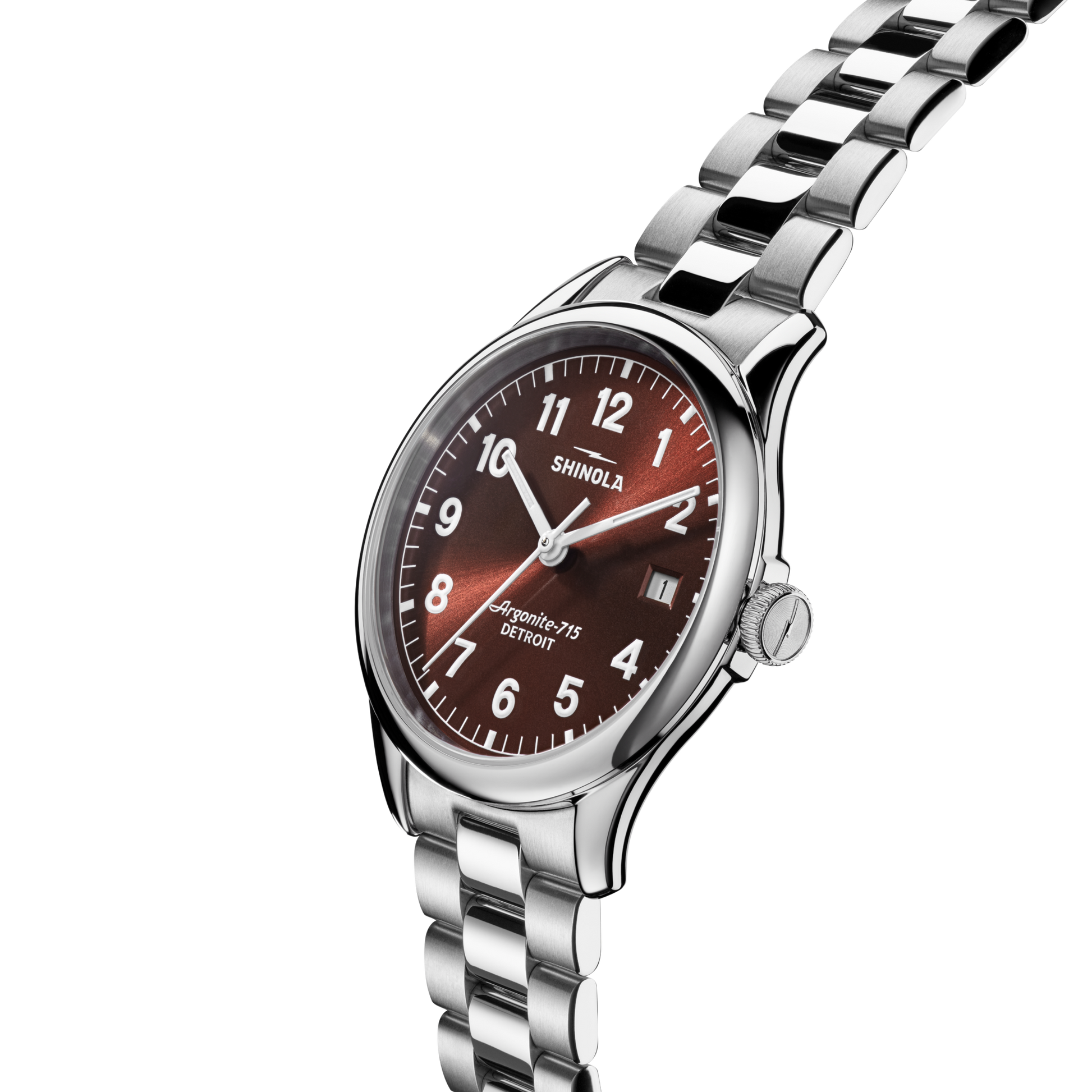 A Shinola Vinton Watch - Whiskey is shown at an angle against a white background, featuring a stainless steel silver bracelet, whiskey-colored dial with white numerals, a date window, and silver hands.