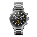 The Shinola Runwell Chronograph West Wind Watch Gift Set features a stainless steel case, black dial with silver hands and yellow accents, three subdials, a metal link bracelet, water resistance to 20 ATM, plus an extra strap. Shown on white.