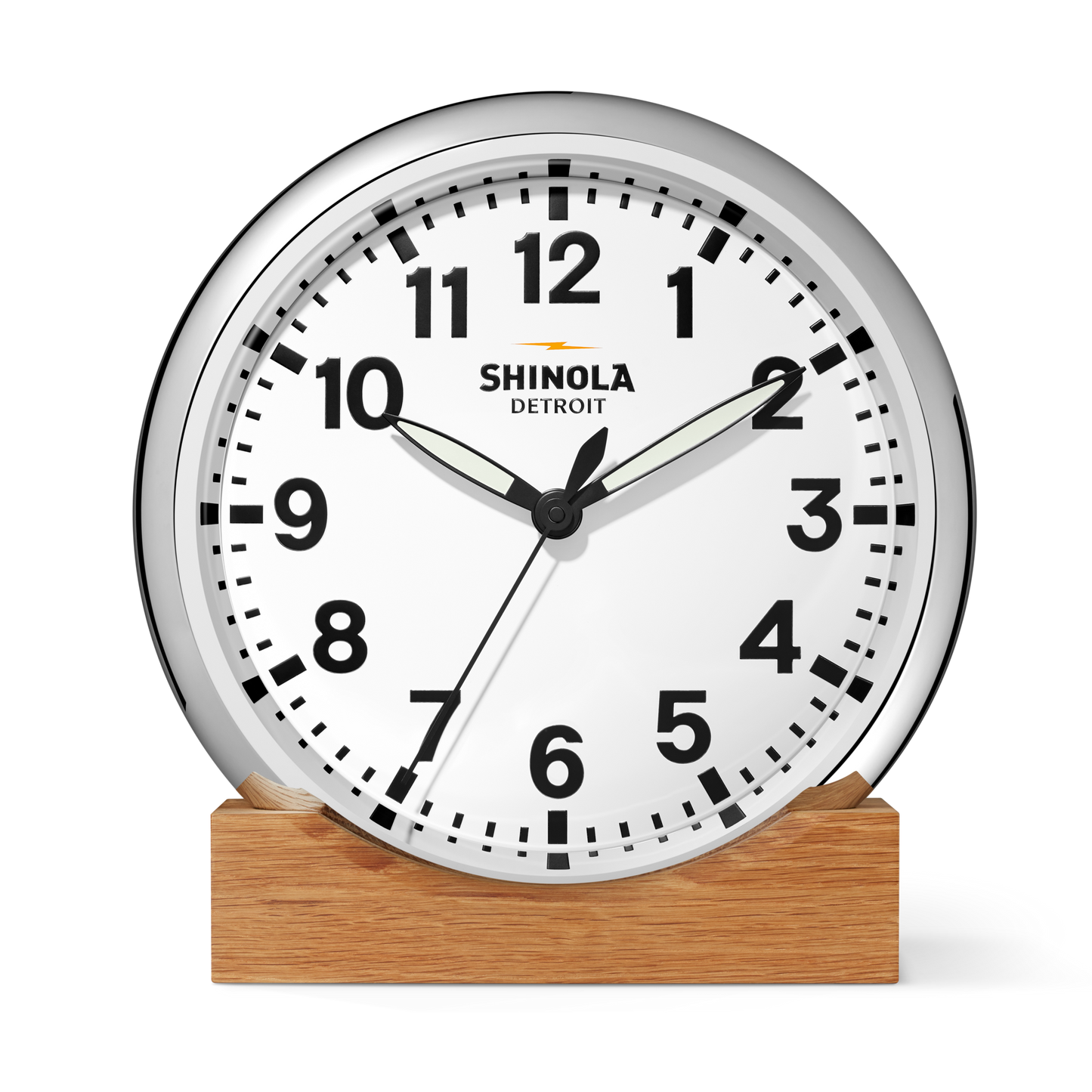 The Shinola 14" Runwell Clock features a white face, black hands and numbers, a chrome casing on a wooden base, and "Shinola Detroit" printed on the dial. It displays the time as 1:50:34.