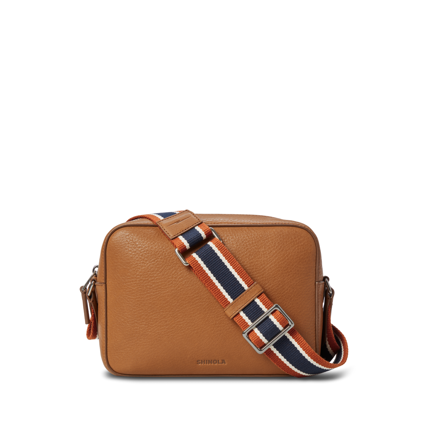 The Camera Crossbody Bag - Tan by Shinola features tan leather, a rectangular shape, silver hardware, a front flap, and an adjustable strap with orange, navy, and white stripes; "Shinola" is stamped near the bottom.