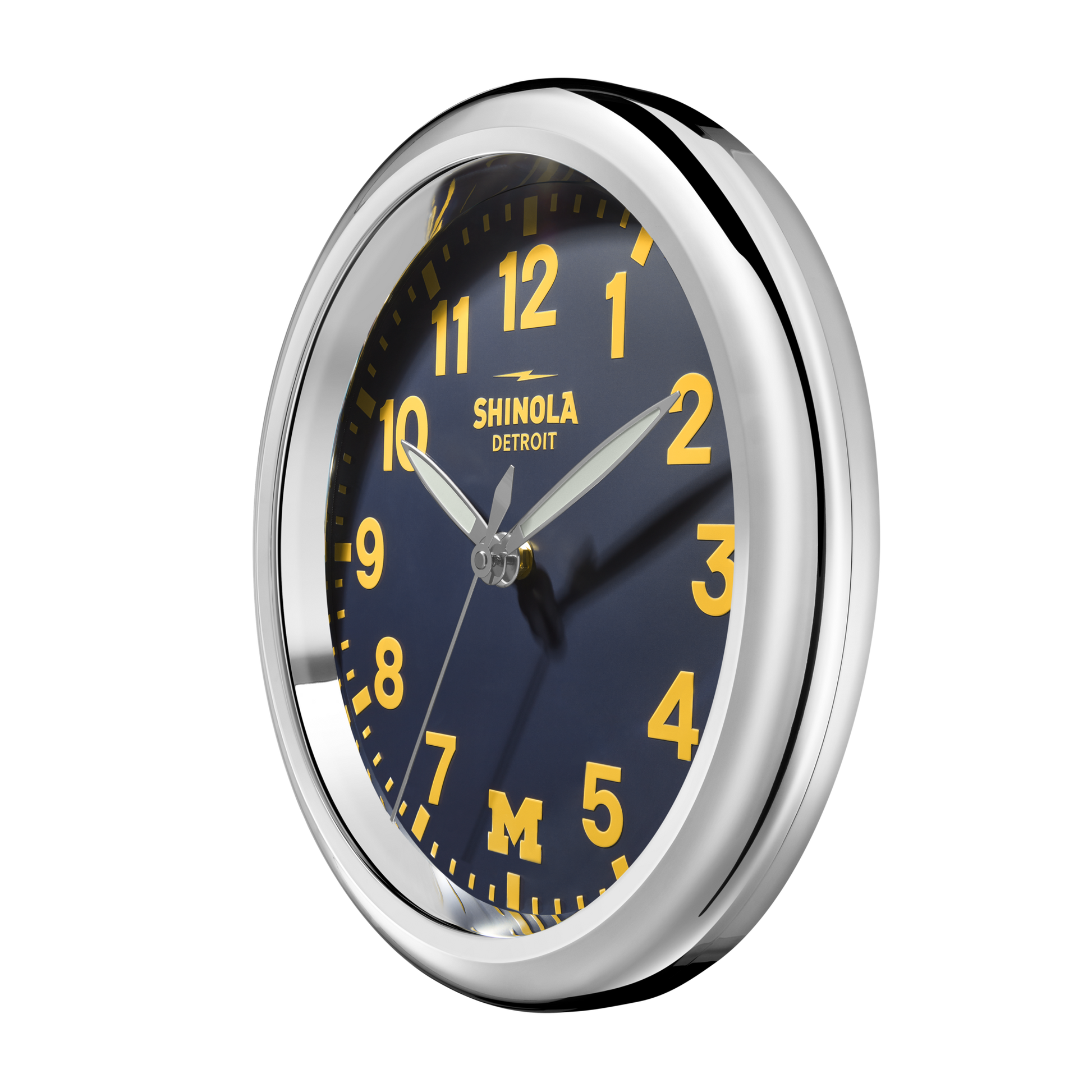 The Shinola 14" Runwell Clock - Blue has a silver frame, navy face, yellow numbers and hands, “SHINOLA DETROIT” at the top, and a yellow “M” at the bottom to represent the University of Michigan.