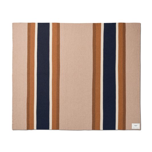 The Shinola Alpaca Throw Blanket in pink and beige is a rectangular blanket featuring wide vertical navy and brown stripes, bordered by thin light brown stripes, with a small white label sewn in one corner.