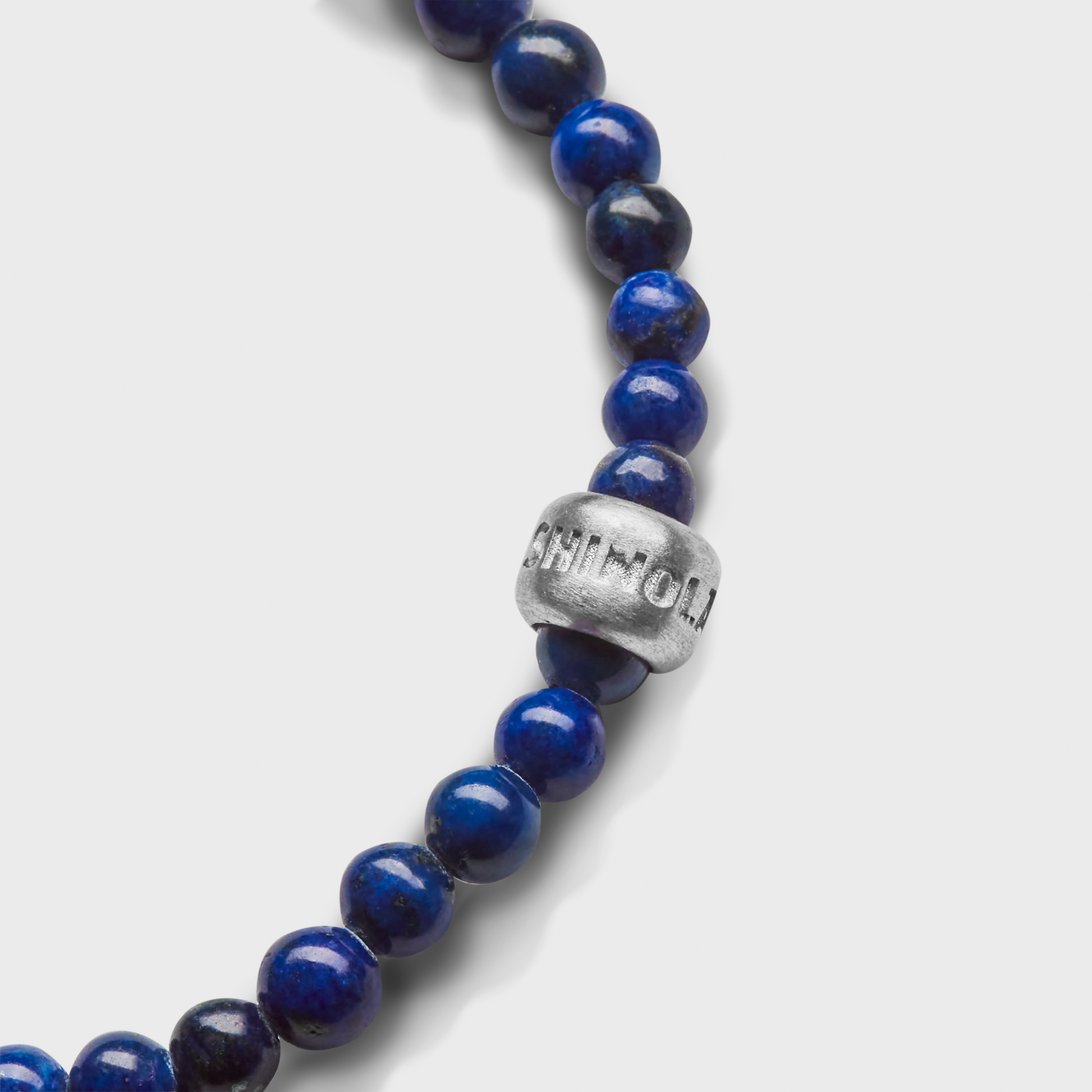 A close-up of the Shinola 4mm Beaded Lapis Bracelet, featuring dark blue round lapis beads and a sterling silver accent engraved with Shinola, photographed on a plain white background to showcase this elegant gemstone accessory.