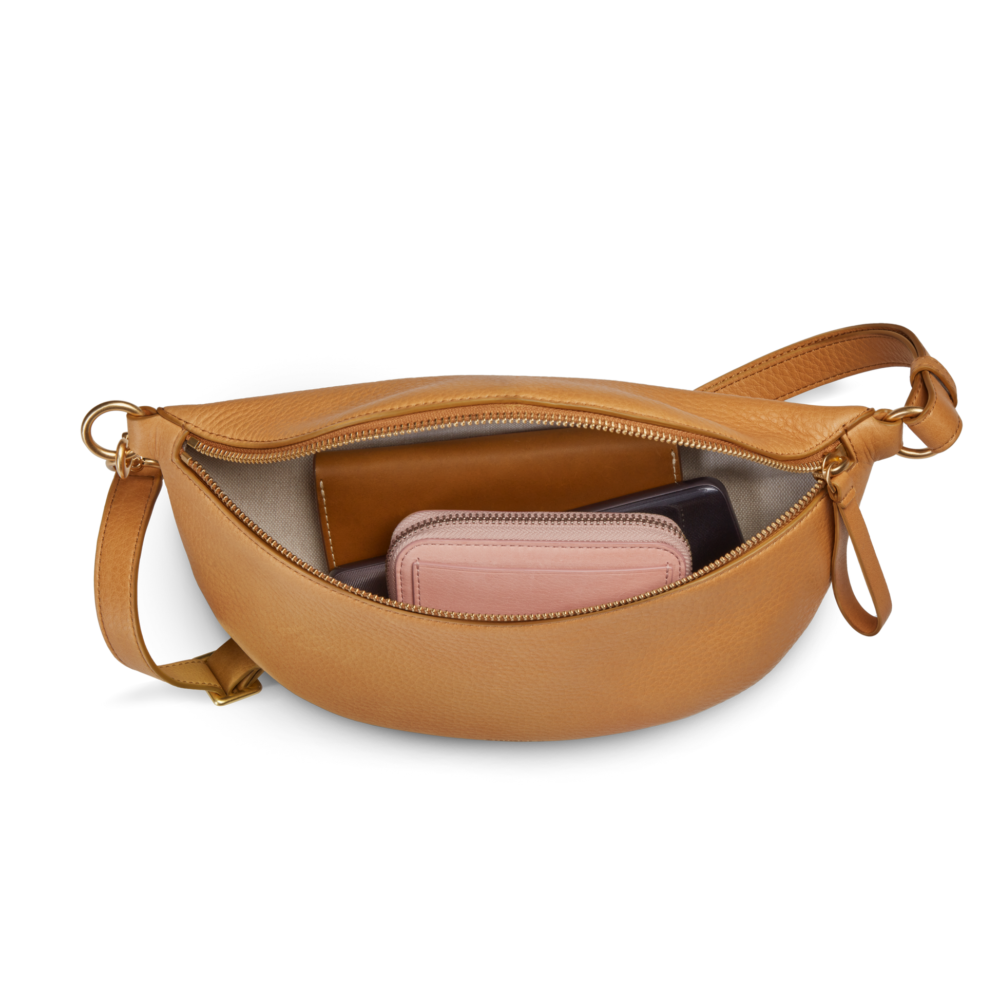 The Shinola Sling Bag - Honey is a tan leather crossbody with an adjustable strap and zippered opening, shown on a white background with a pink wallet and a dark item—possibly another wallet or phone—inside.