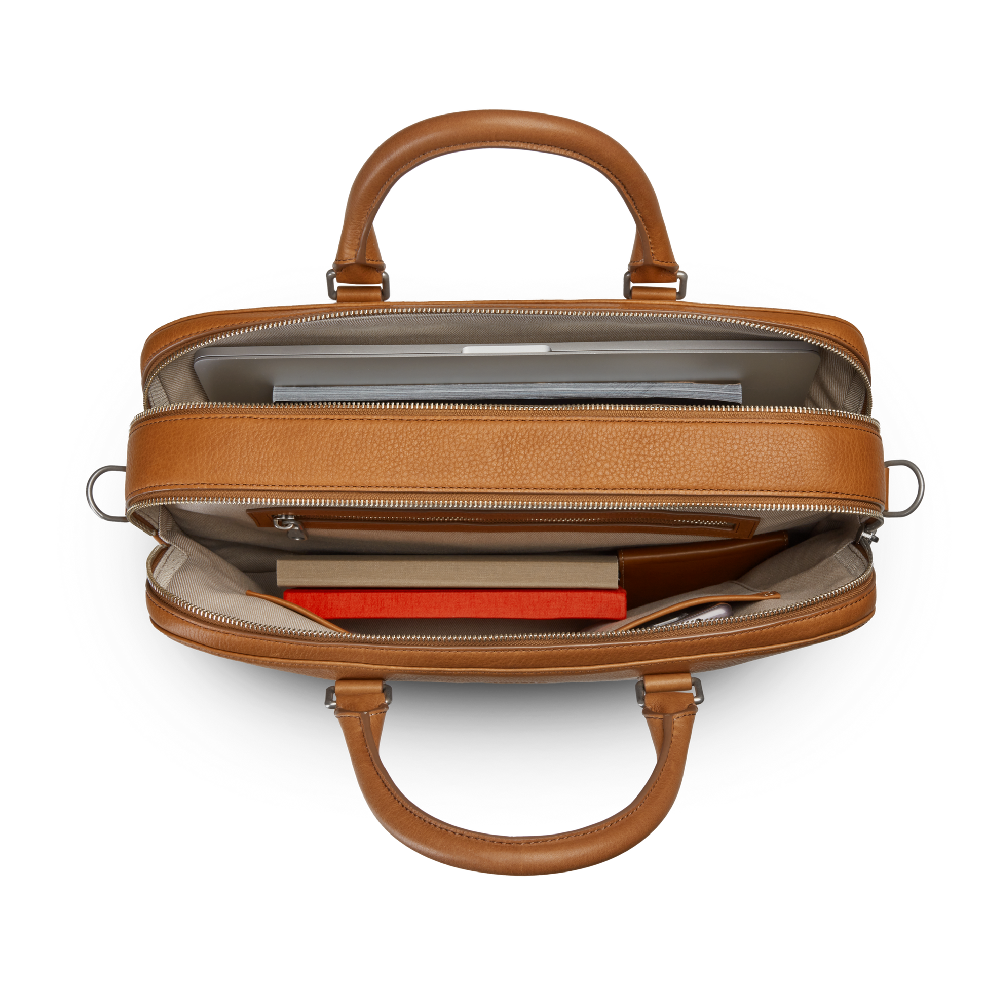 Top view of an open Shinola Double Zip Briefcase - Tan, with a laptop, notebook, orange book, and small accessories neatly organized in separate compartments, plus an extra compartment for added storage.