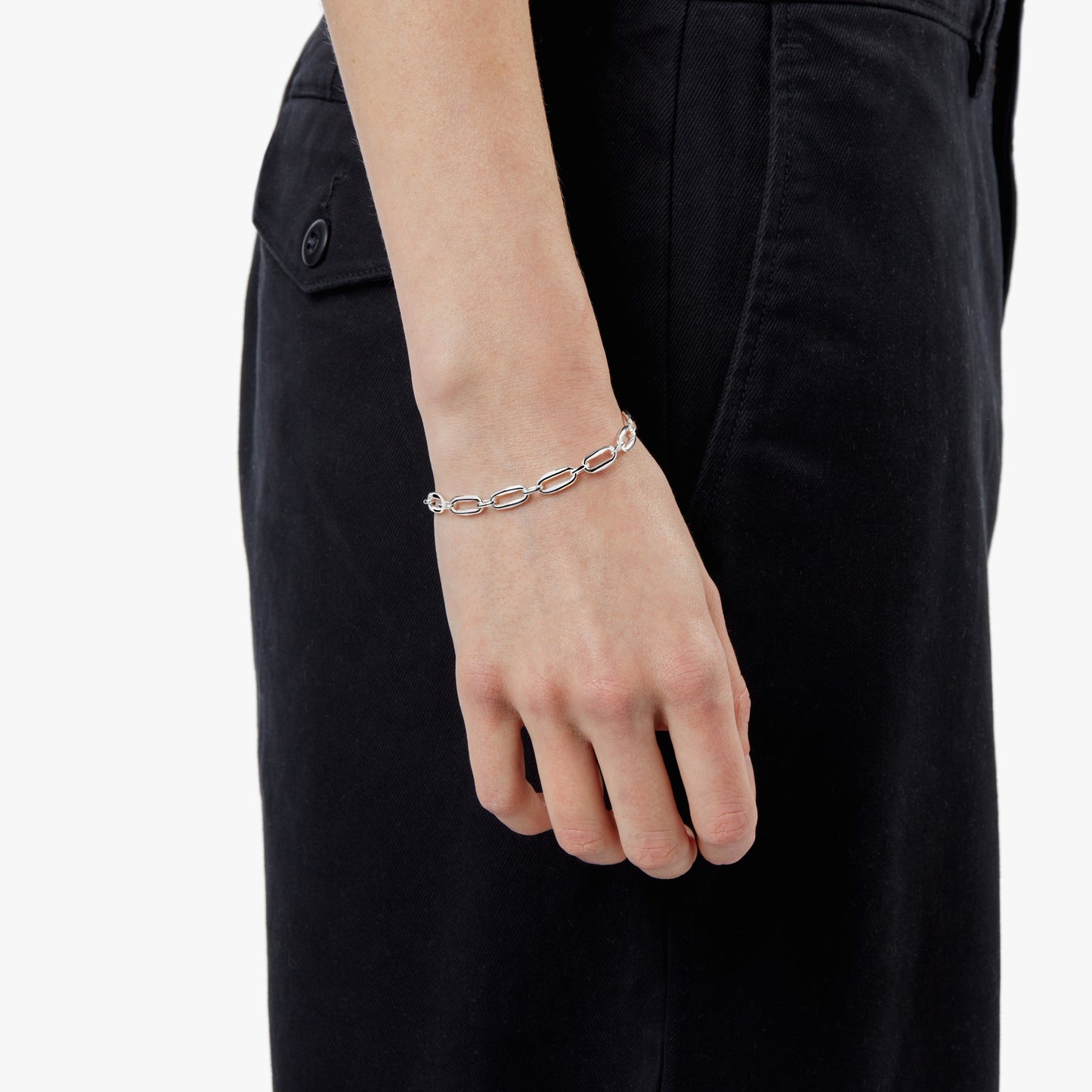 A close-up of a person’s hand wearing the Shinola Signature Link Bracelet - Sterling Silver, with their arm resting against dark pants and a white background.