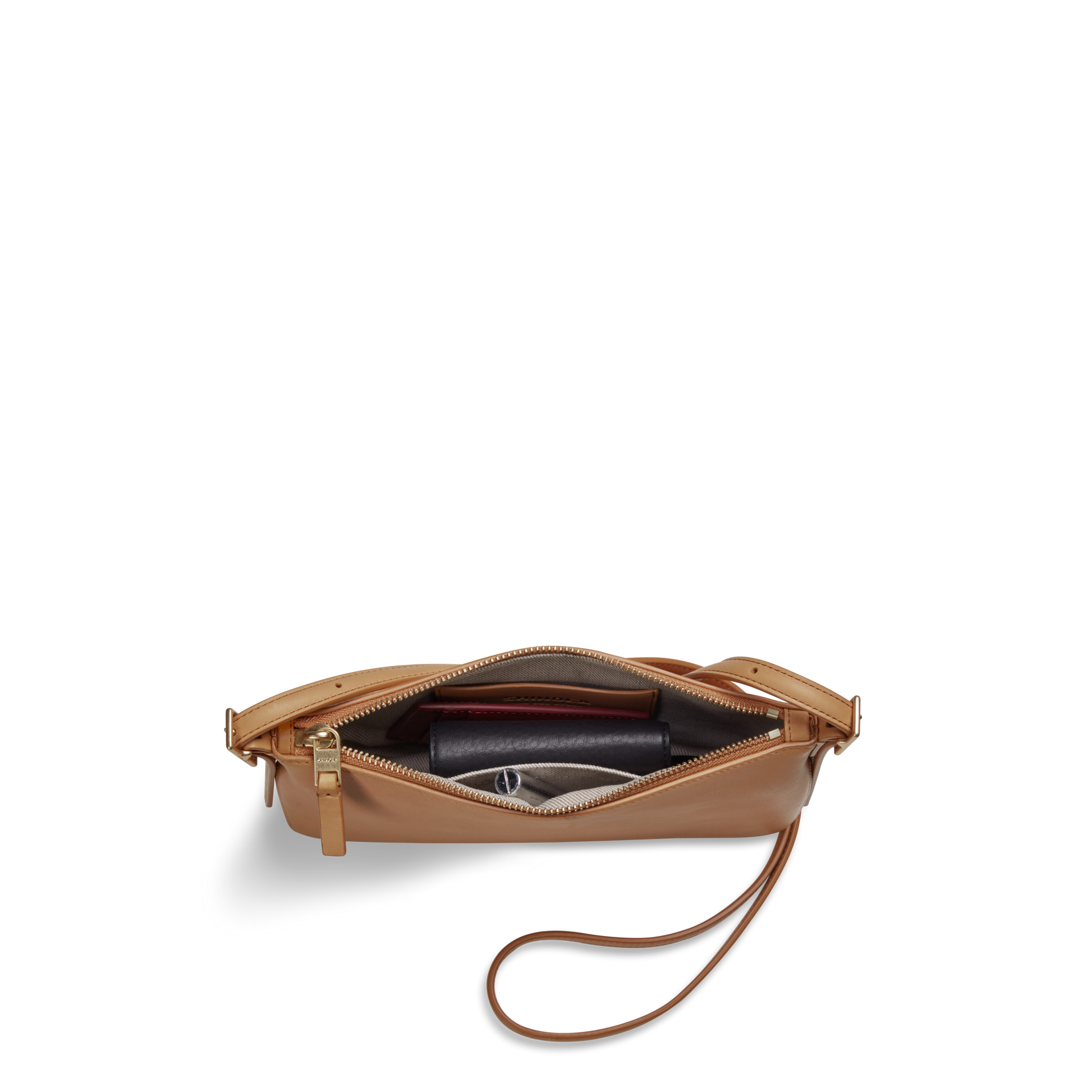 The Shinola Small Bixby Crossbody in Honey, crafted from tan natural leather, is pictured from above with its zipper open, revealing a maroon wallet and round item inside—a stylish everyday accessory.