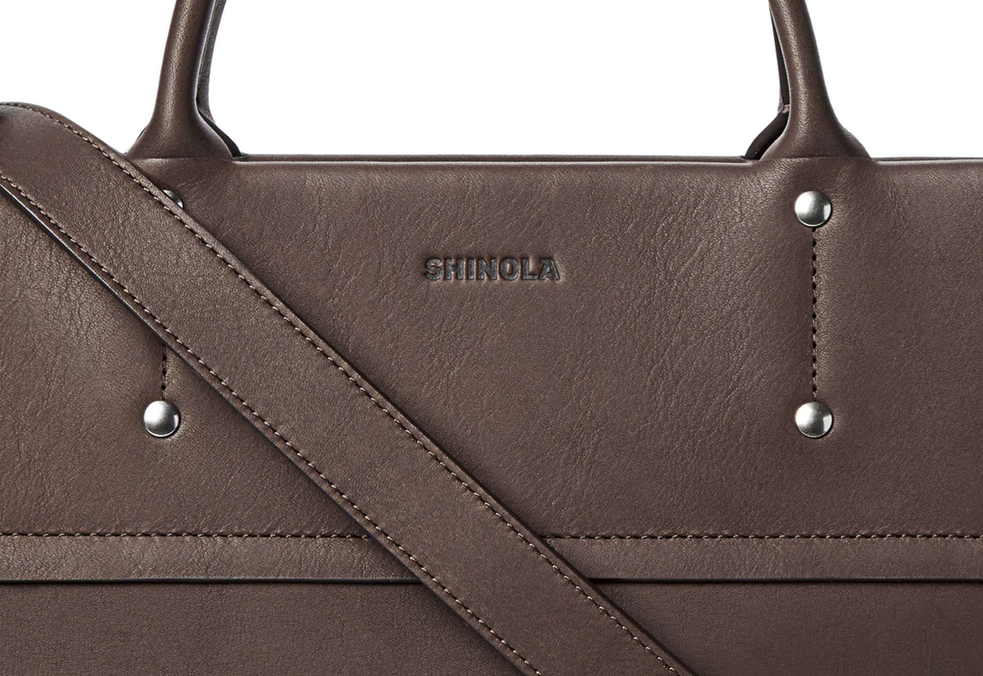 Close-up of the Shinola Day Satchel - Espresso, featuring brown leather with silver rivets, detailed stitching, and a front strap. "Shinola" is embossed near the top center, showcasing its stylish design as the perfect on-the-go bag.