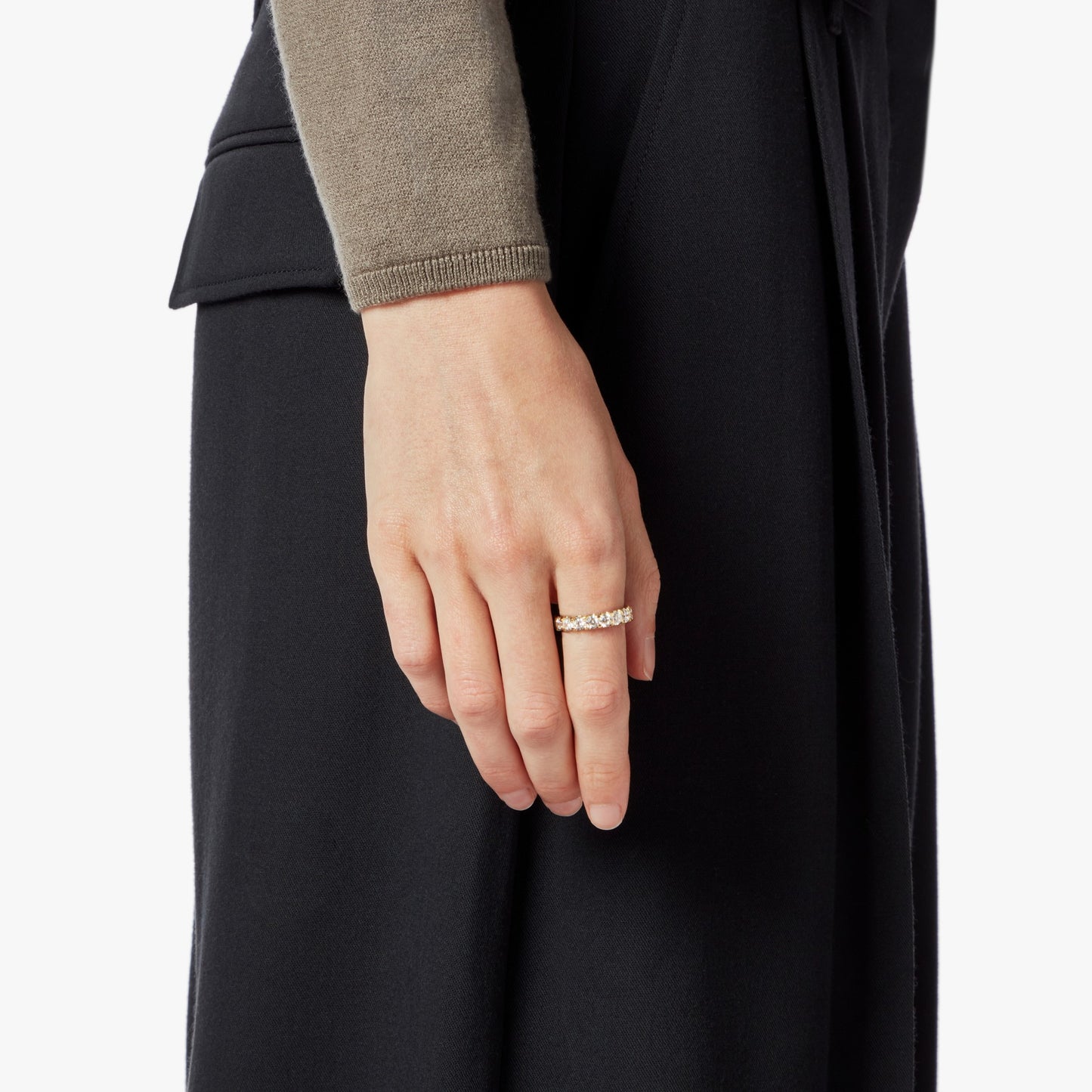 A person in a tan long-sleeve top and black skirt or pants wears the Shinola 2 Carat Diamond Anniversary Band YG on their left hand, standing against a plain white background.