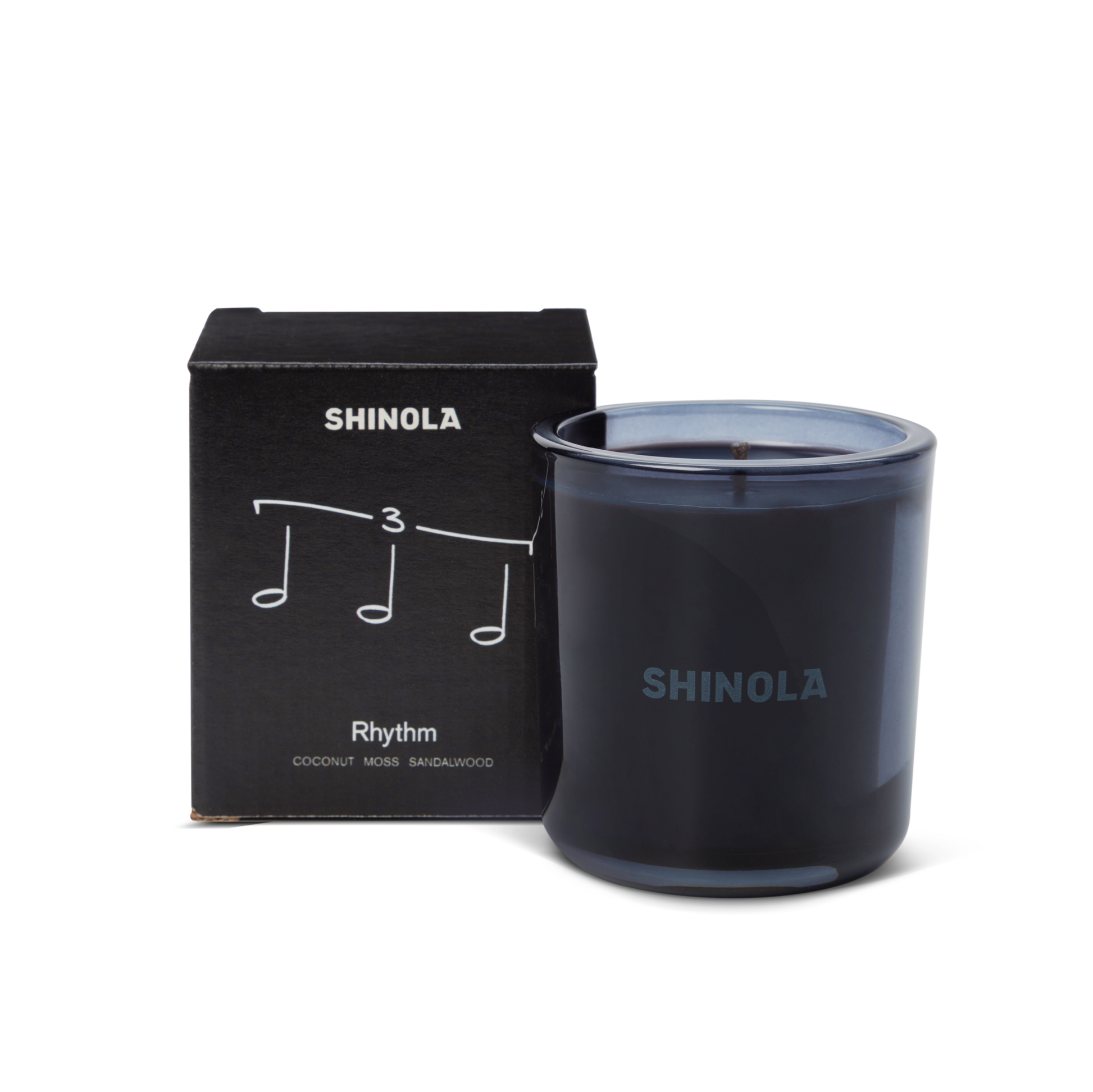 The Shinola Rhythm 8 oz Scented Candle sits next to its box decorated with musical notes and "Rhythm," inspired by Detroit nightlife. Scented with coconut, moss, and sandalwood, the candle comes in a recycled glass vessel.