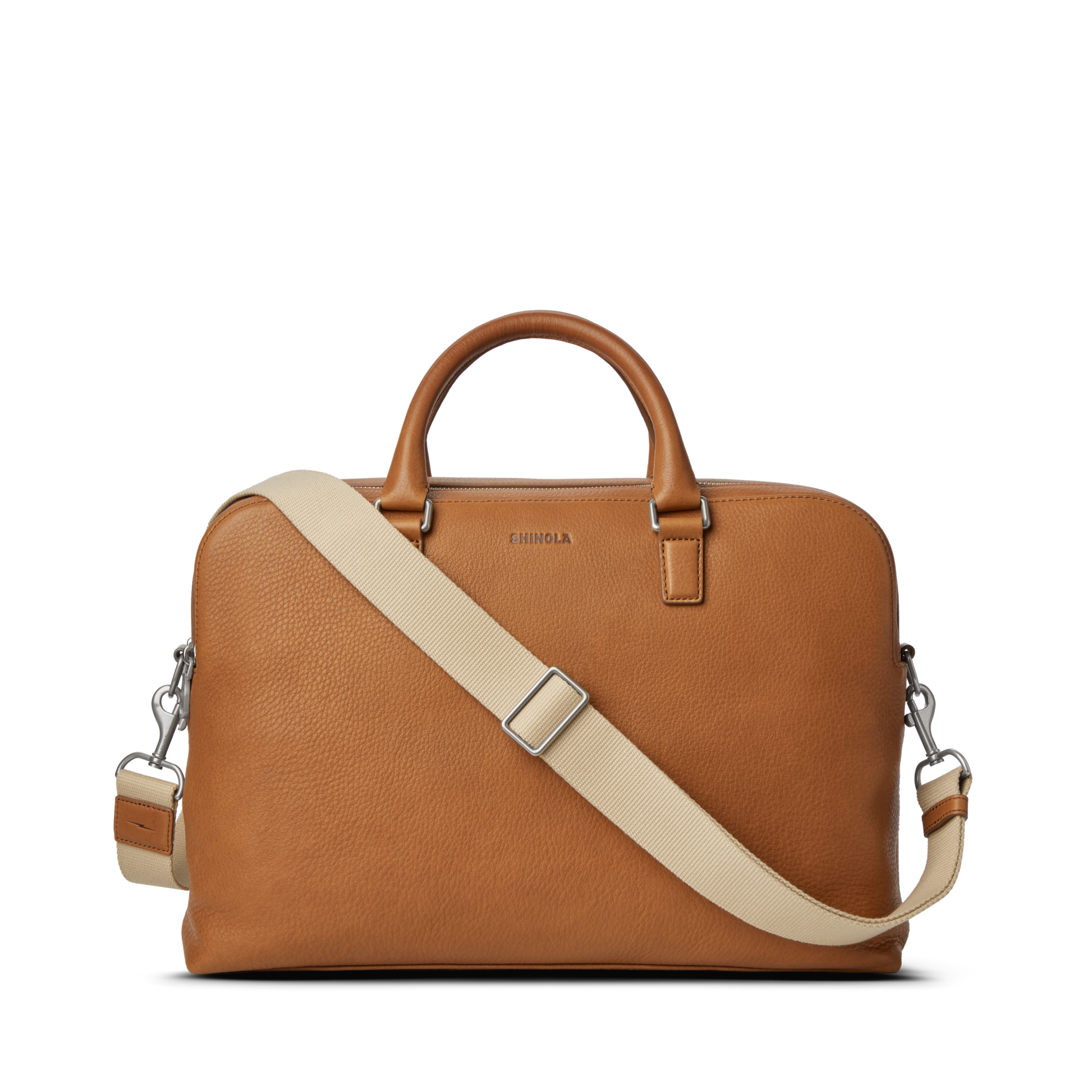The Shinola Double Zip Briefcase - Tan, crafted from natural grain leather, features short handles, a detachable beige shoulder strap, an extra compartment, silver hardware, and a simple elegant design against a white background.