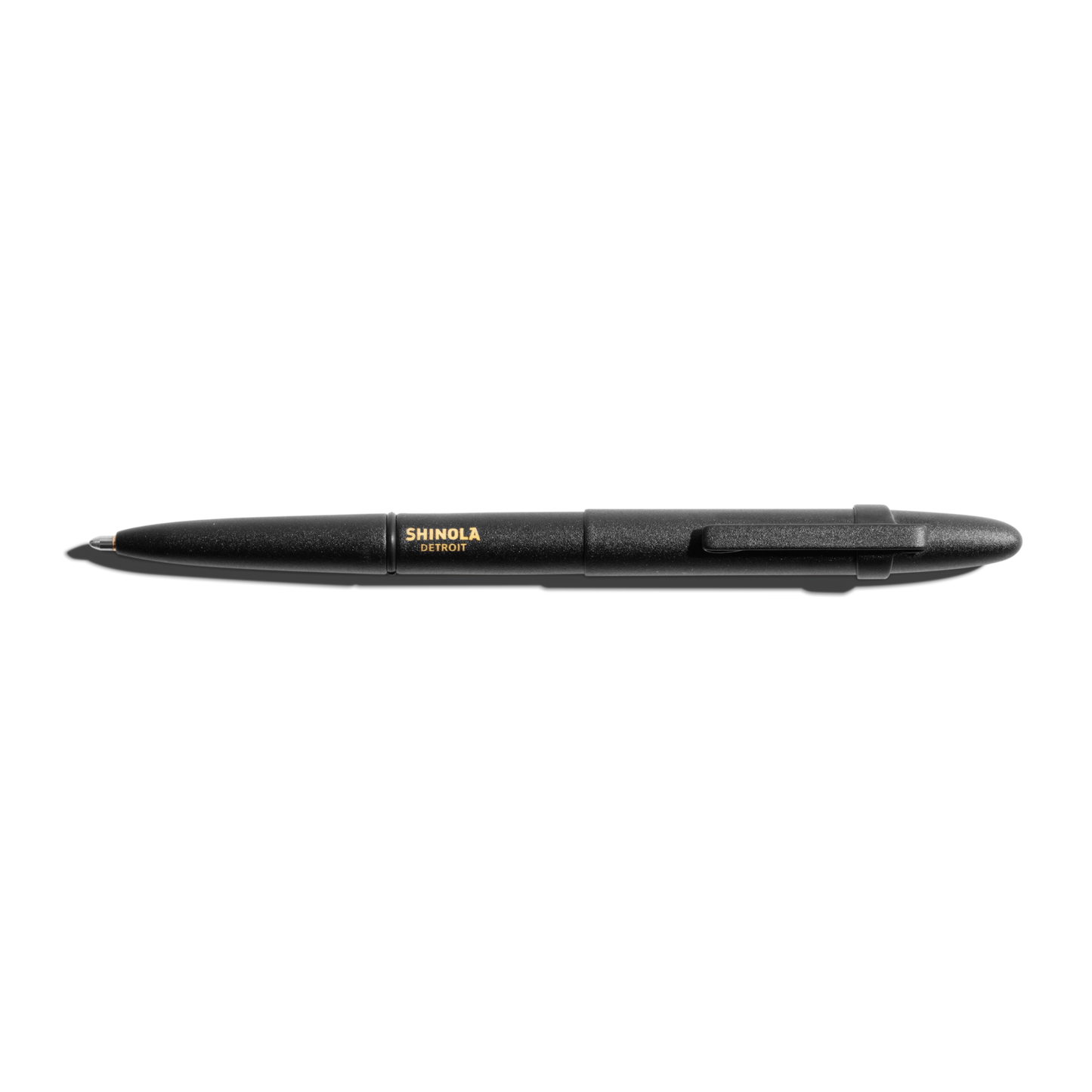 The Shinola + Fisher Bullet Space Pen - Matte Black, with gold SHINOLA DETROIT branding and a clip, is shown against a white background—designed to write underwater and in extreme conditions.