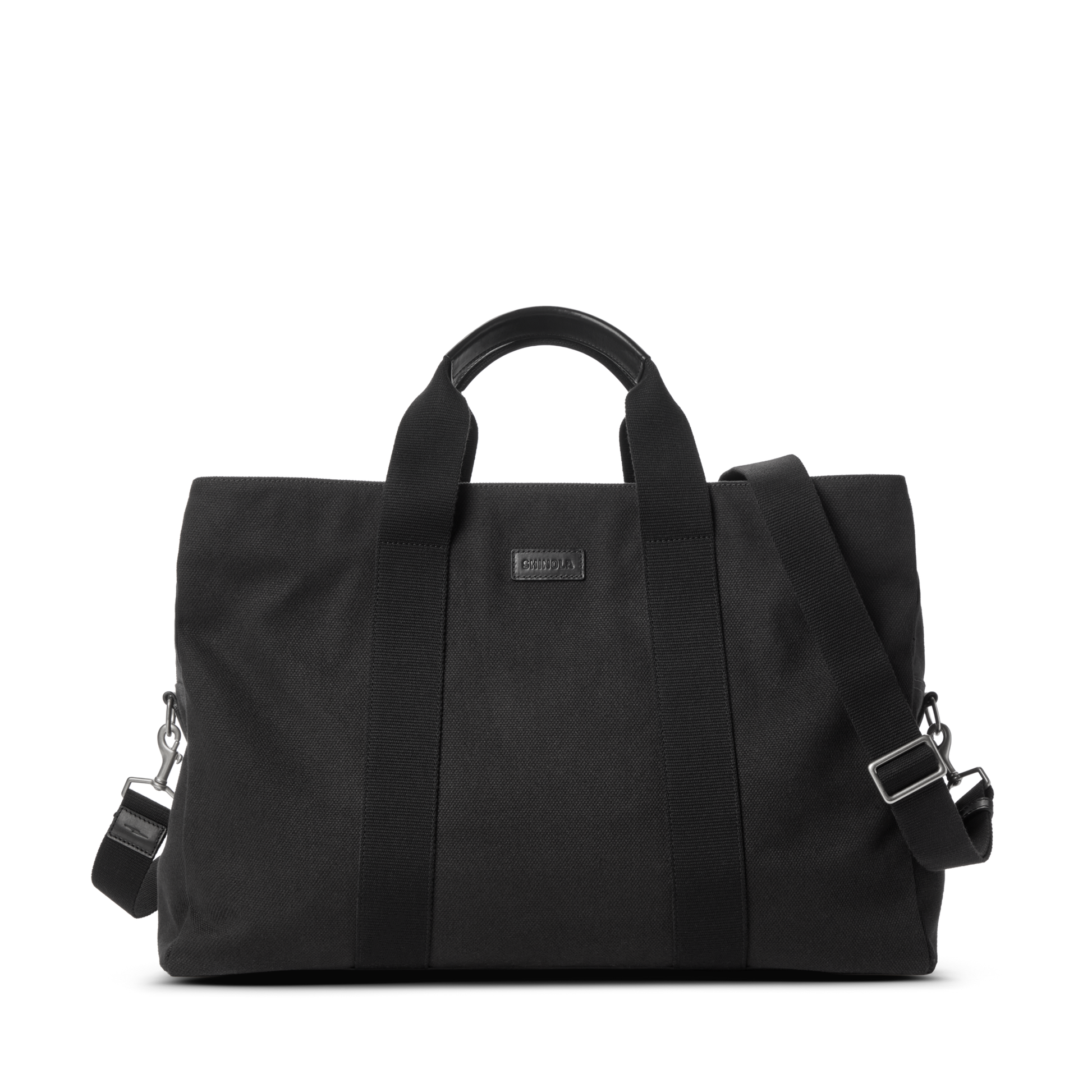 The Shinola Runwell Canvas Duffle Bag - Black features two short handles, a detachable adjustable shoulder strap, and metal hardware—a stylish TSA carry-on or travel duffle, shown against a plain white background.