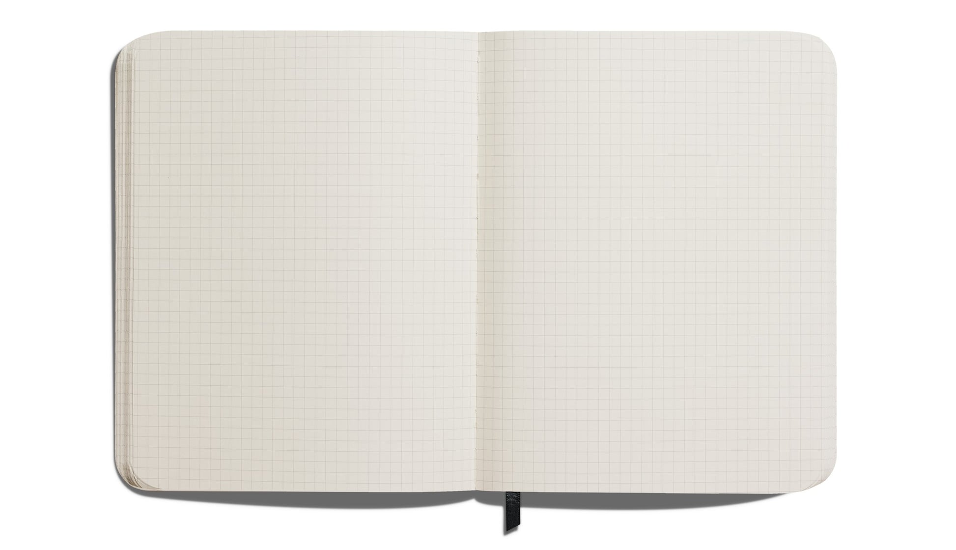 An overhead view of the Shinola Large Hard Grid Journal in black shows its blank grid pages and black ribbon bookmark, highlighting its quality craftsmanship. Made with acid-free paper, it features a hard linen cover on a plain white background.