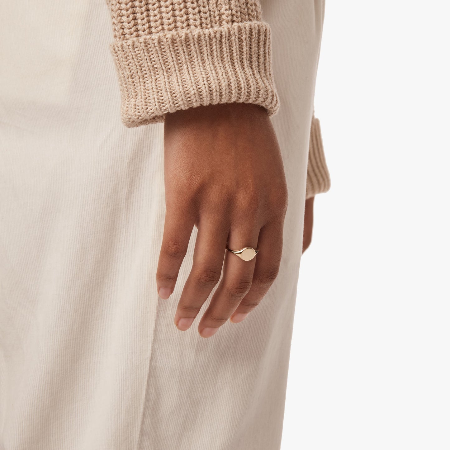 A close-up of a hand wearing Shinola's Petite Round Signet Ring - Yellow Gold, styled with a beige knit sleeve and light pants, highlights the ring’s effortless, timeless appeal.