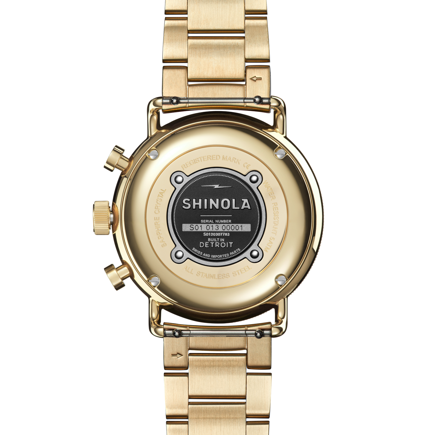A close-up of the back of a silver Shinola Canfield Sport Chronograph Watch, showing its serial number, assembly details, and Built in Detroit text, with a metallic link bracelet and two buttons on the left side.