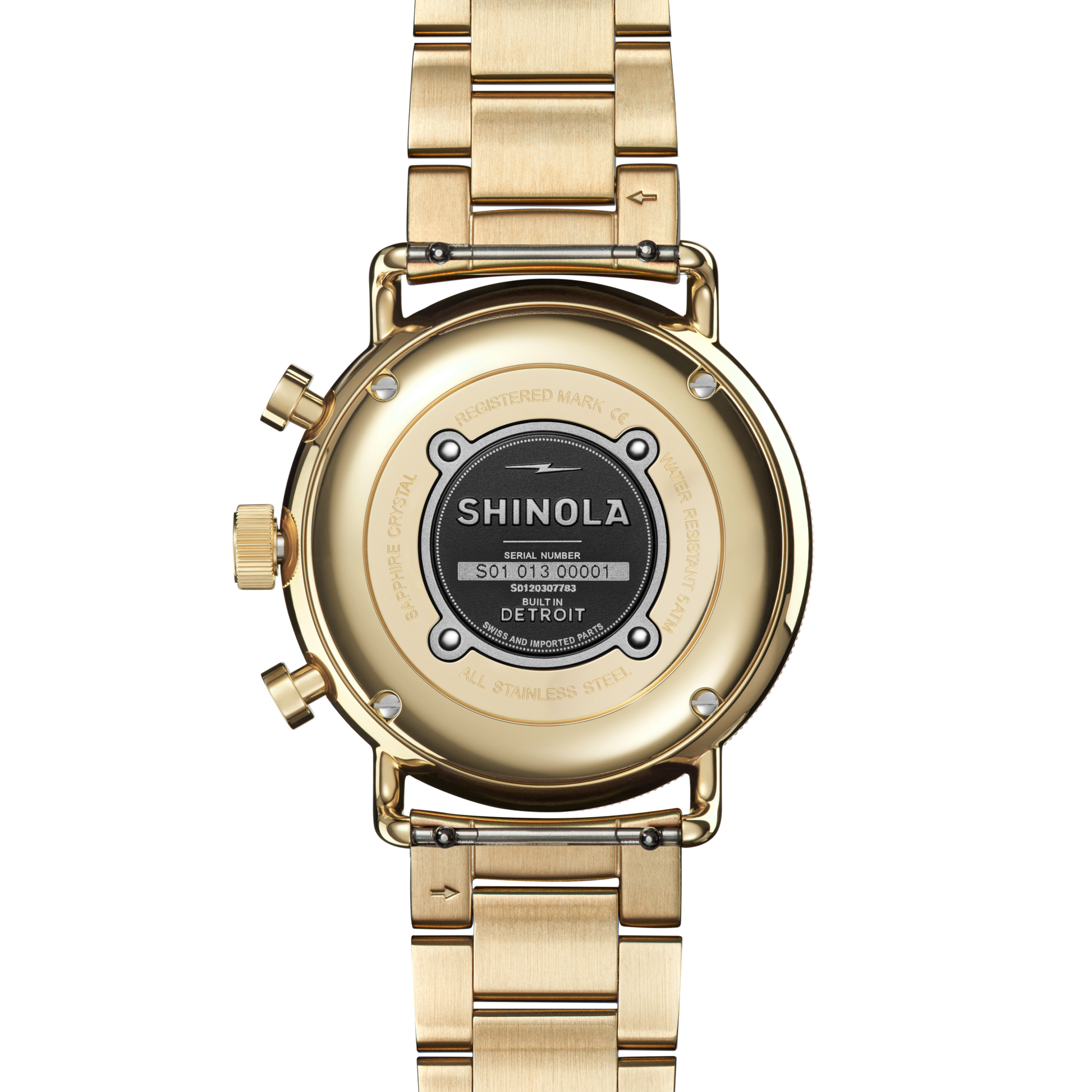 A close-up of the back of a silver Shinola Canfield Sport Chronograph Watch, showing its serial number, assembly details, and Built in Detroit text, with a metallic link bracelet and two buttons on the left side.