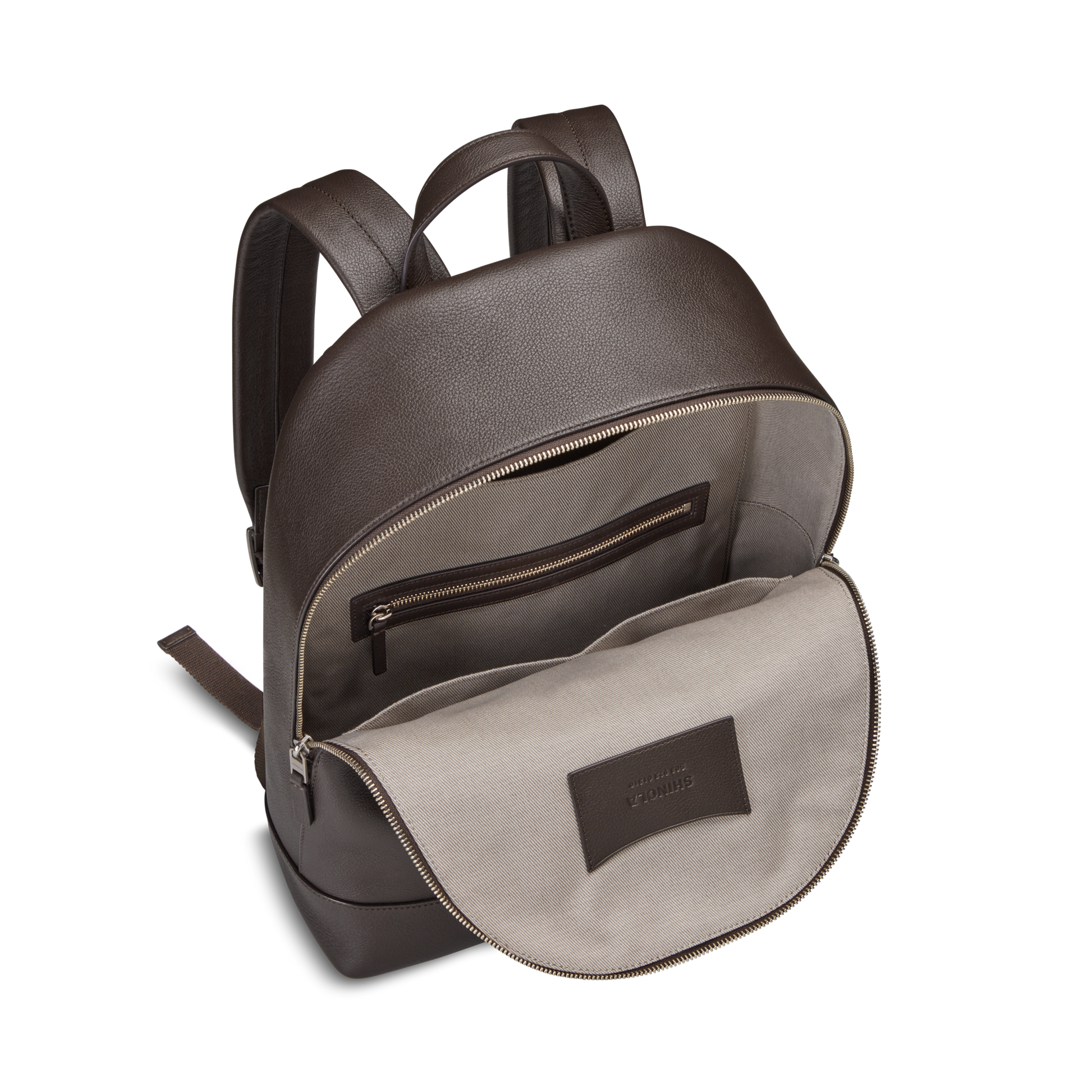 The Shinola Canfield Backpack - Espresso features brown leather, adjustable straps, and a light beige fabric interior with a zippered pocket and stitched leather label.