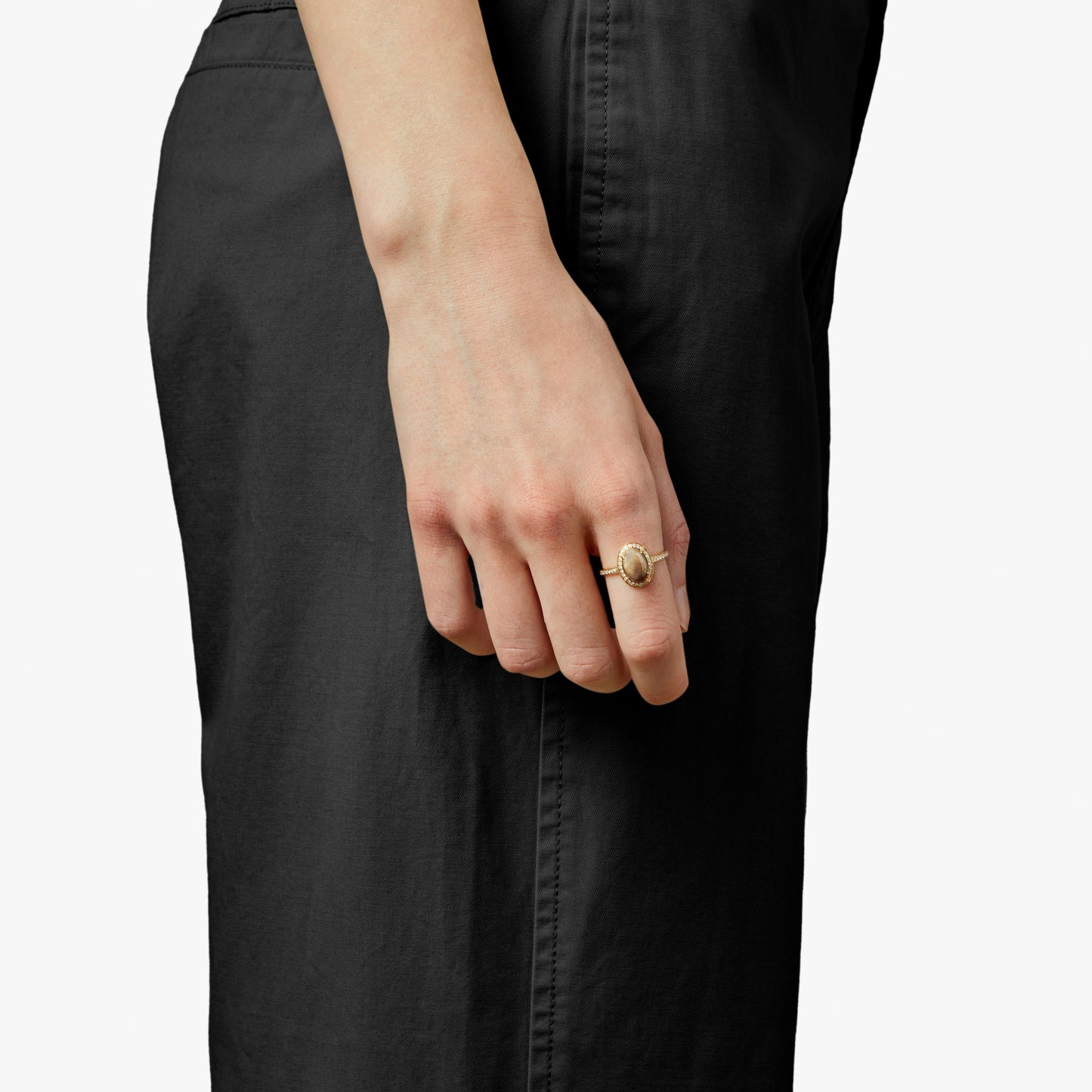 A person in black pants is shown from the waist down, their hand at their side wearing the Shinola Petite Diamond Pave Petoskey Oval Ring in yellow gold, with a plain white background.