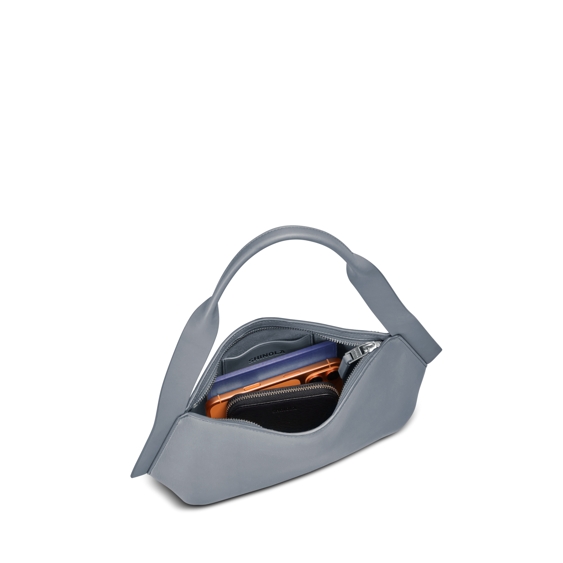 The Small Derby Shoulder Bag - Mist by Shinola is a light gray, naturally crafted leather bag with a curved handle, open to show a wallet, smartphone, and zipped pouch inside against a white background.