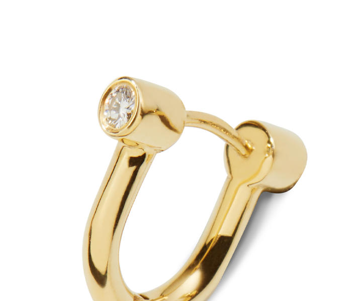 A close-up of Shinola's Diamond Bike Lock Huggie Earrings in yellow gold, featuring a single round diamond at one end of the U-shaped design, displayed against a plain white background.