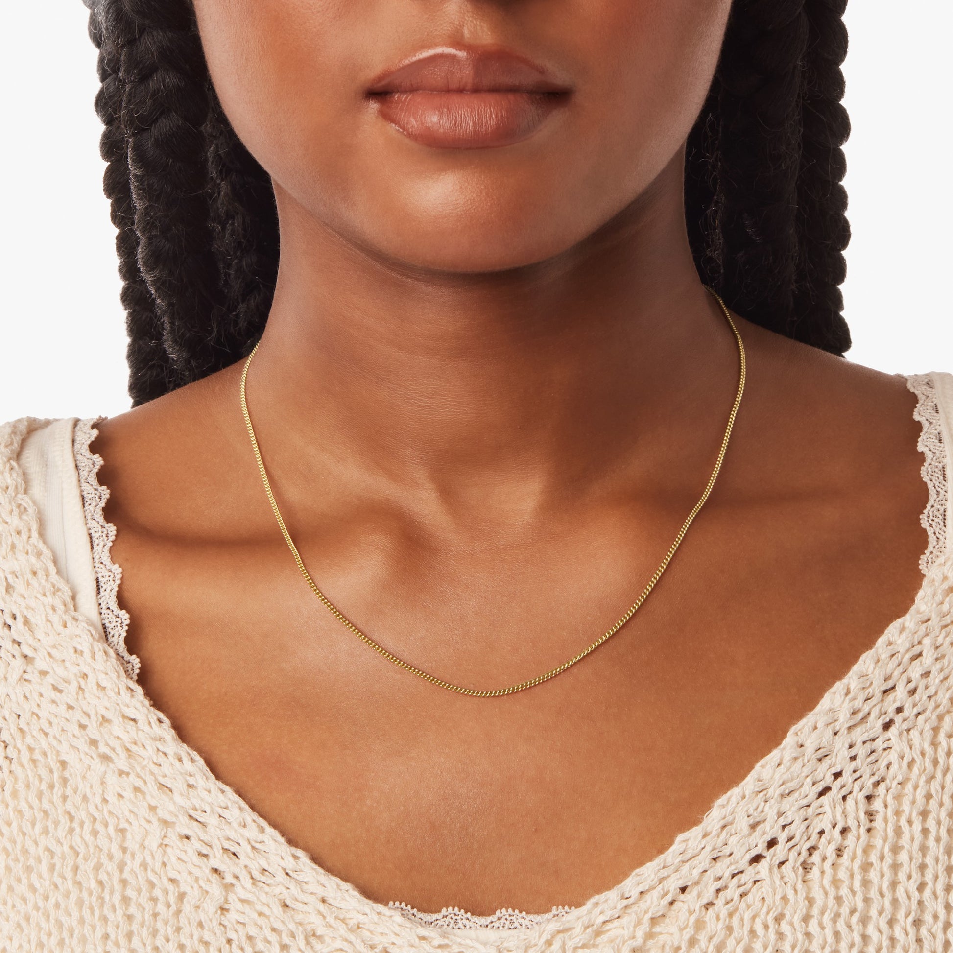 A woman with braided hair wears the Shinola Small Curb Link necklace in 14k yellow gold and a cream knit top over a white lace-trimmed shirt, shown from shoulders to chin against a plain background.