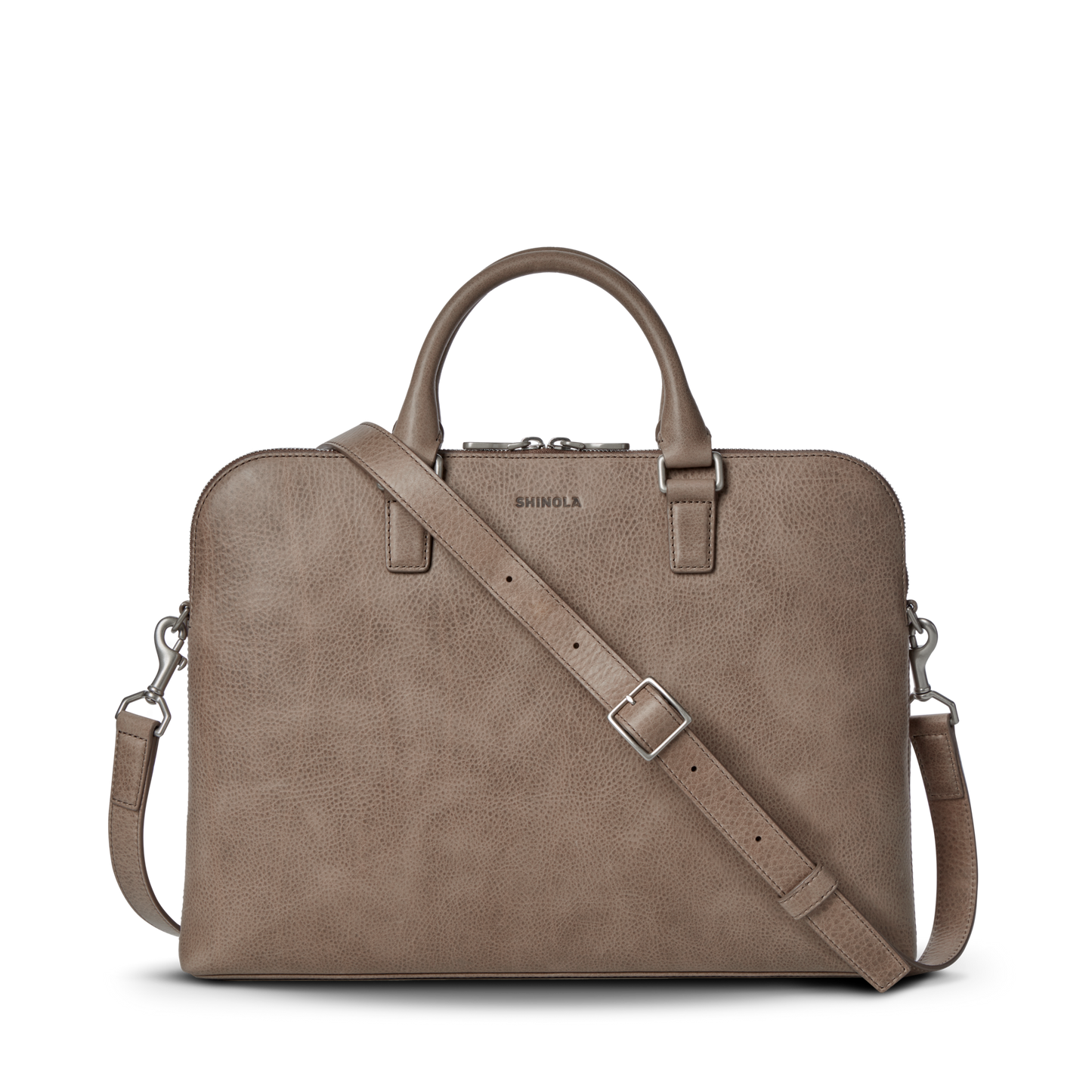 The Shinola Portfolio Briefcase - Stone is shown on a white background. Made of taupe leather, it features two top handles, a detachable adjustable shoulder strap, zipper closure, and an embossed Shinola logo above the zipper.