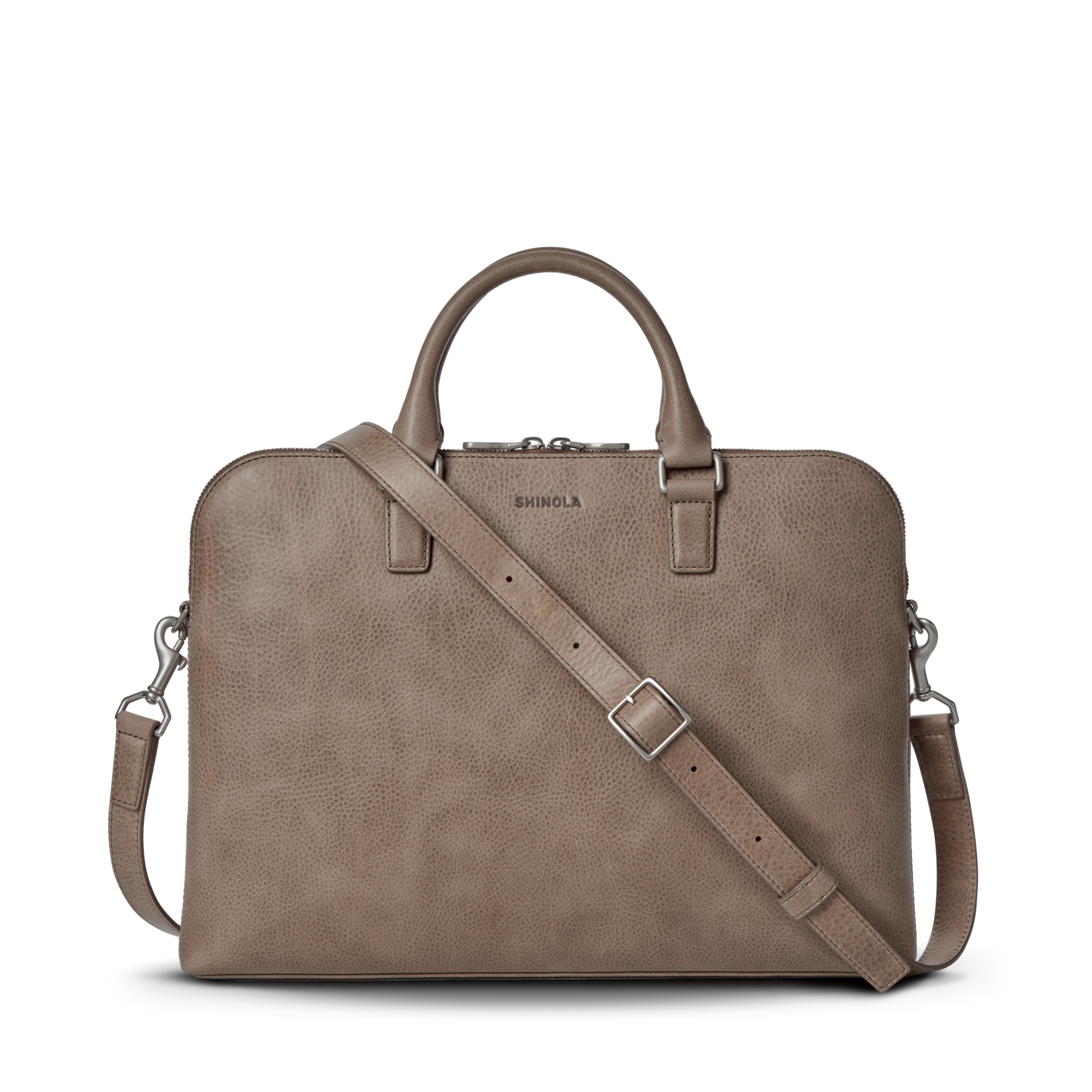 The Shinola Portfolio Briefcase - Stone is shown on a white background. Made of taupe leather, it features two top handles, a detachable adjustable shoulder strap, zipper closure, and an embossed Shinola logo above the zipper.