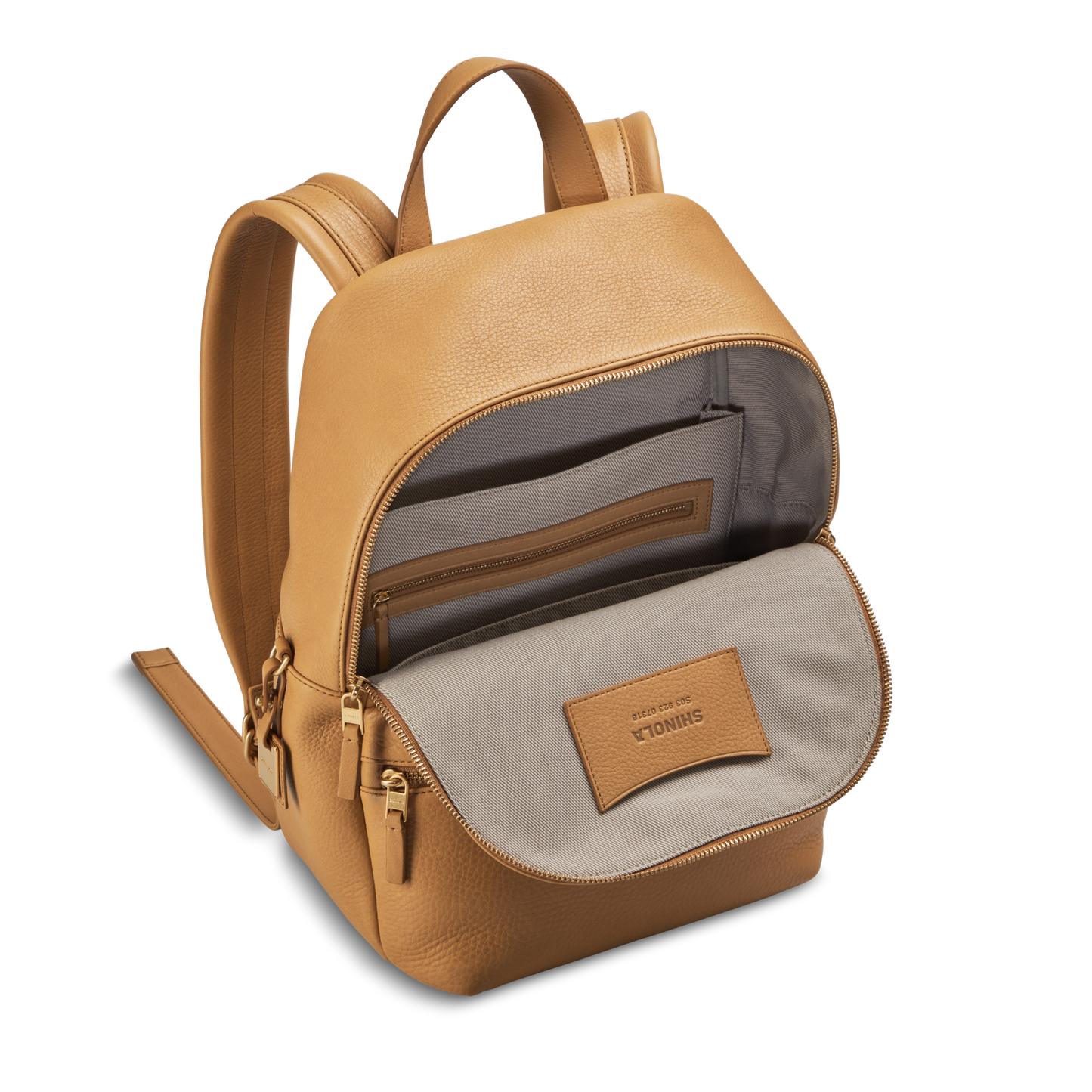 The Shinola Small Runwell Backpack in Honey features Natural Grain Leather, a beige interior, open main compartment, inner zip pocket, small logo patch under the front flap, padded straps, and gold zippers—perfect for stylish portability.
